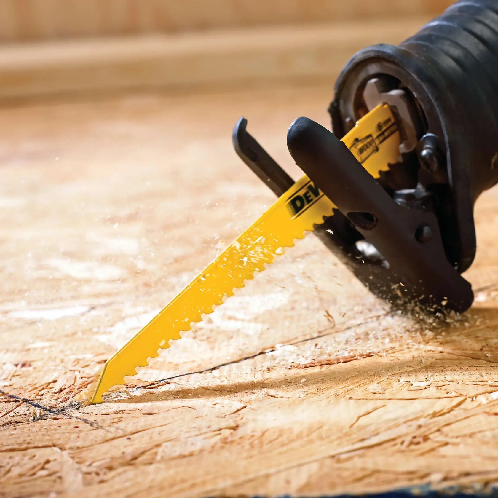 Close-up of a yellow DEWALT reciprocating saw blade cutting through a piece of wood, with sawdust flying.