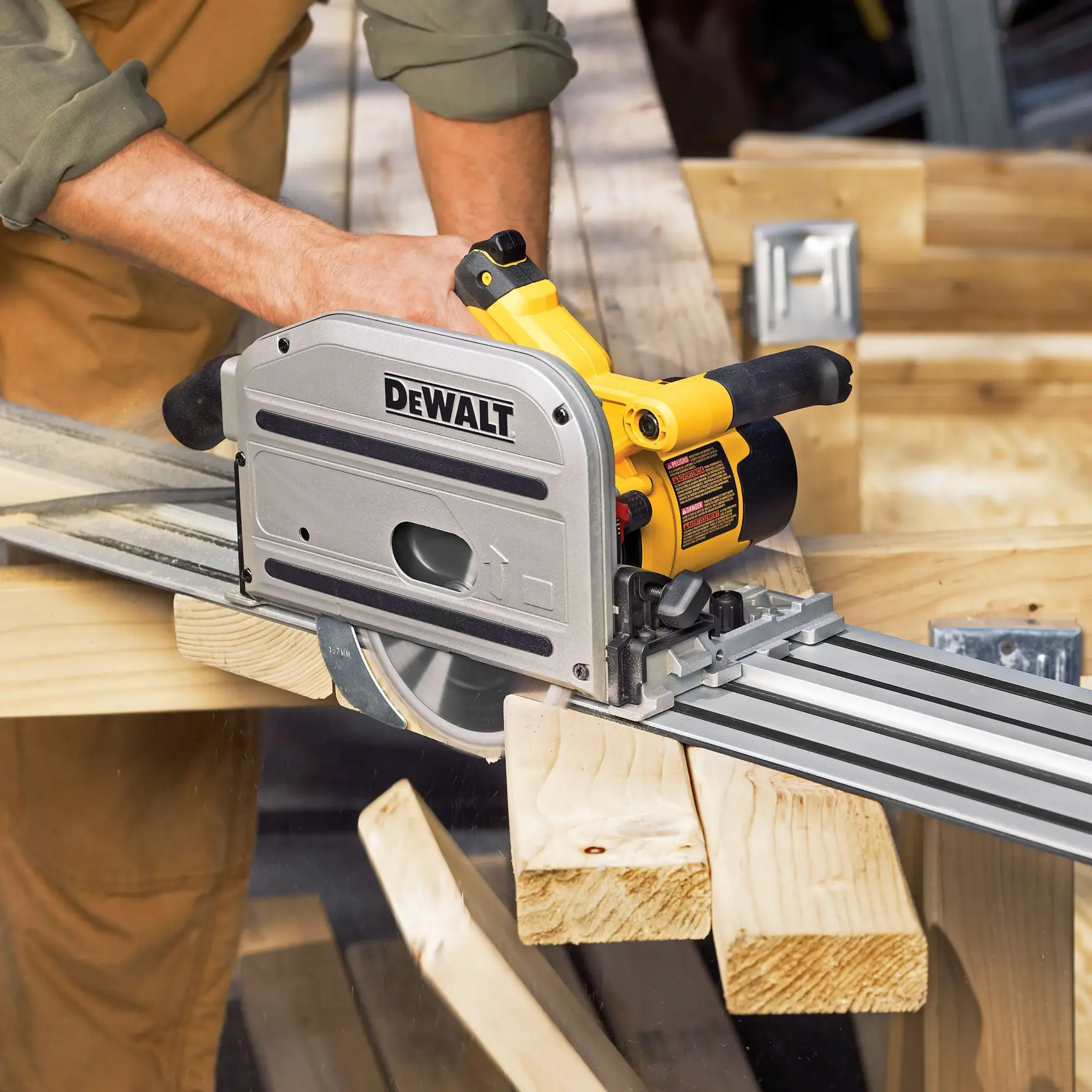 A person uses a DEWALT track saw to cut wooden boards in a workshop. The saw is positioned on a metal track, providing straight and precise cuts.