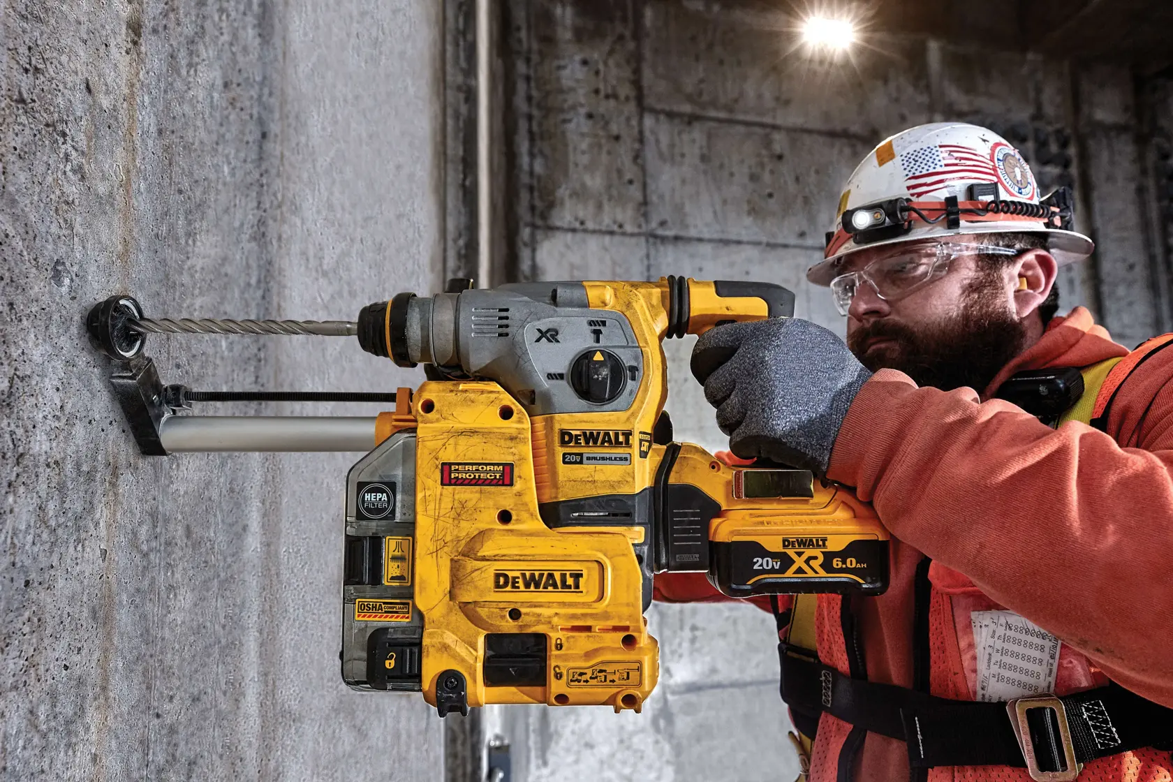 A construction worker wearing safety gear uses a yellow DEWALT cordless rotary hammer drill with a dust extraction attachment on a concrete wall.