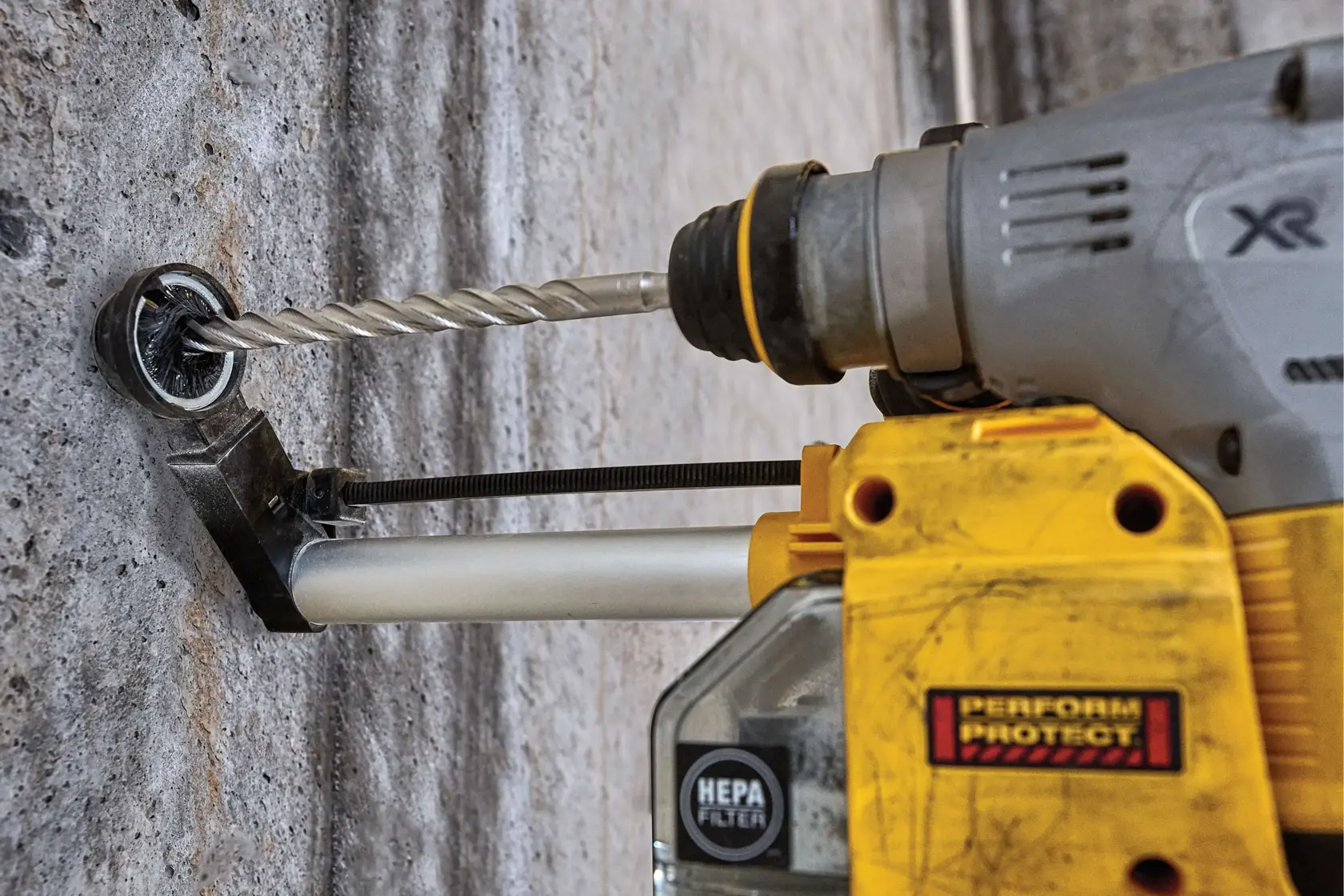 Close-up of a DEWALT power drill with a dust collection attachment and HEPA filter drilling into a concrete wall.