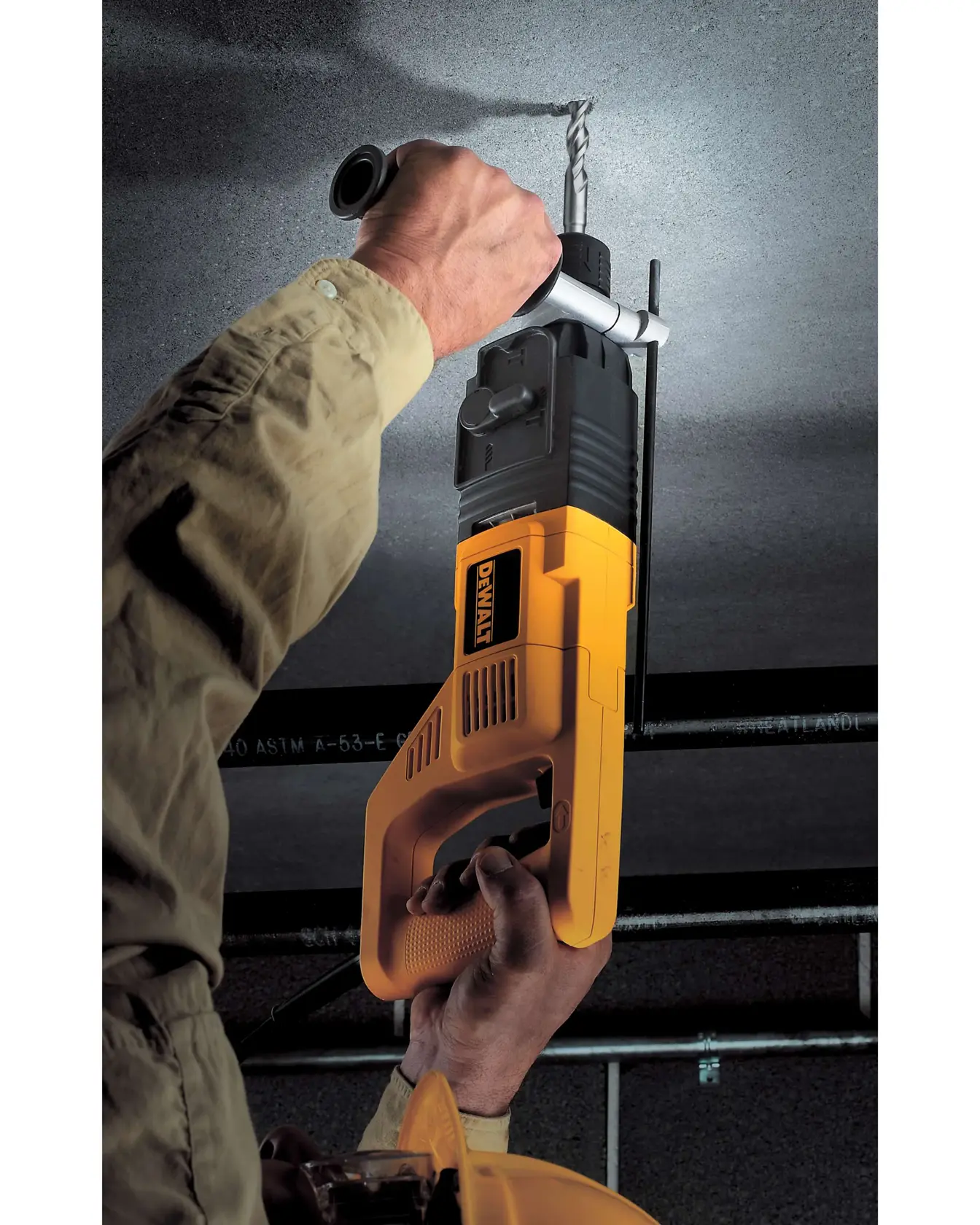 A person using a DEWALT power drill to drill into a ceiling. The drill is yellow and black, and the person is wearing a long-sleeve shirt and a safety helmet.