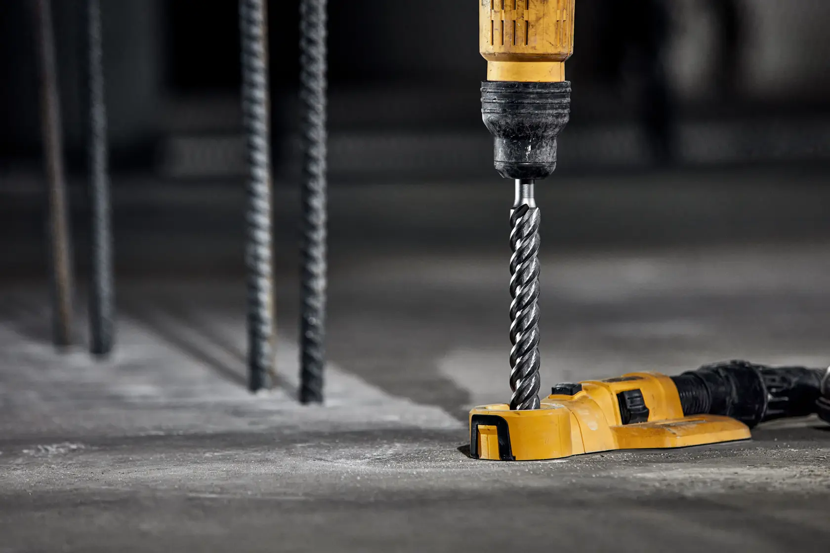 A close-up of a DEWALT drill being used to bore into a concrete surface, with rebar rods visible in the background.