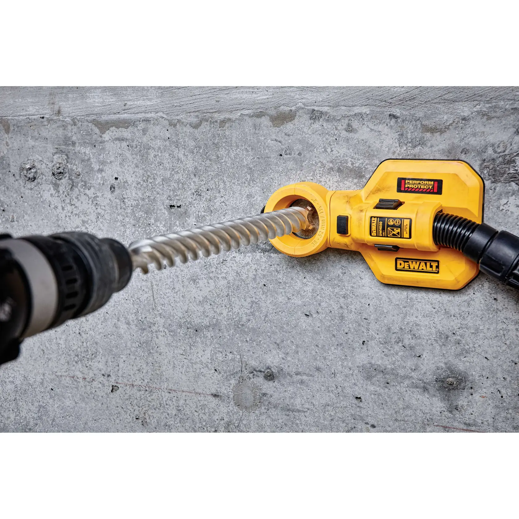 A DEWALT dust extraction attachment connected to a drill with a spiral bit, being used to drill into a concrete surface.