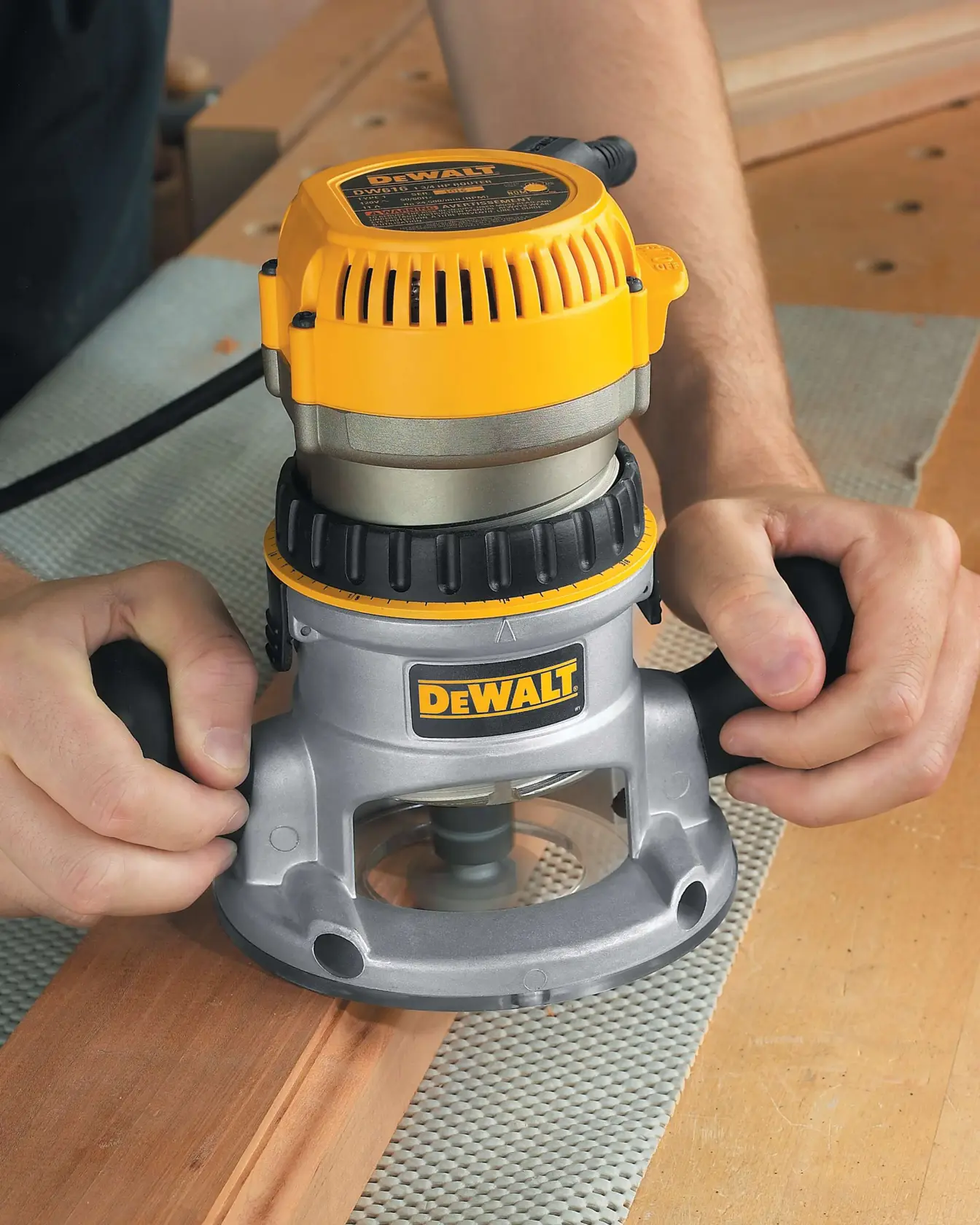 A close-up view of a person using a DEWALT DW616 wood router on a piece of wood in a workshop.