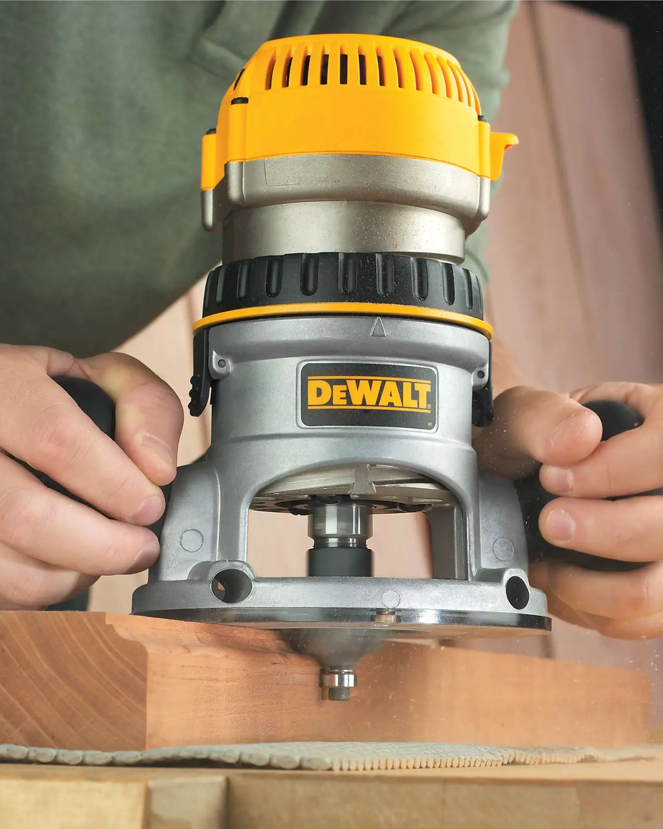 A person using a DEWALT wood router to shape the edge of a wooden board.