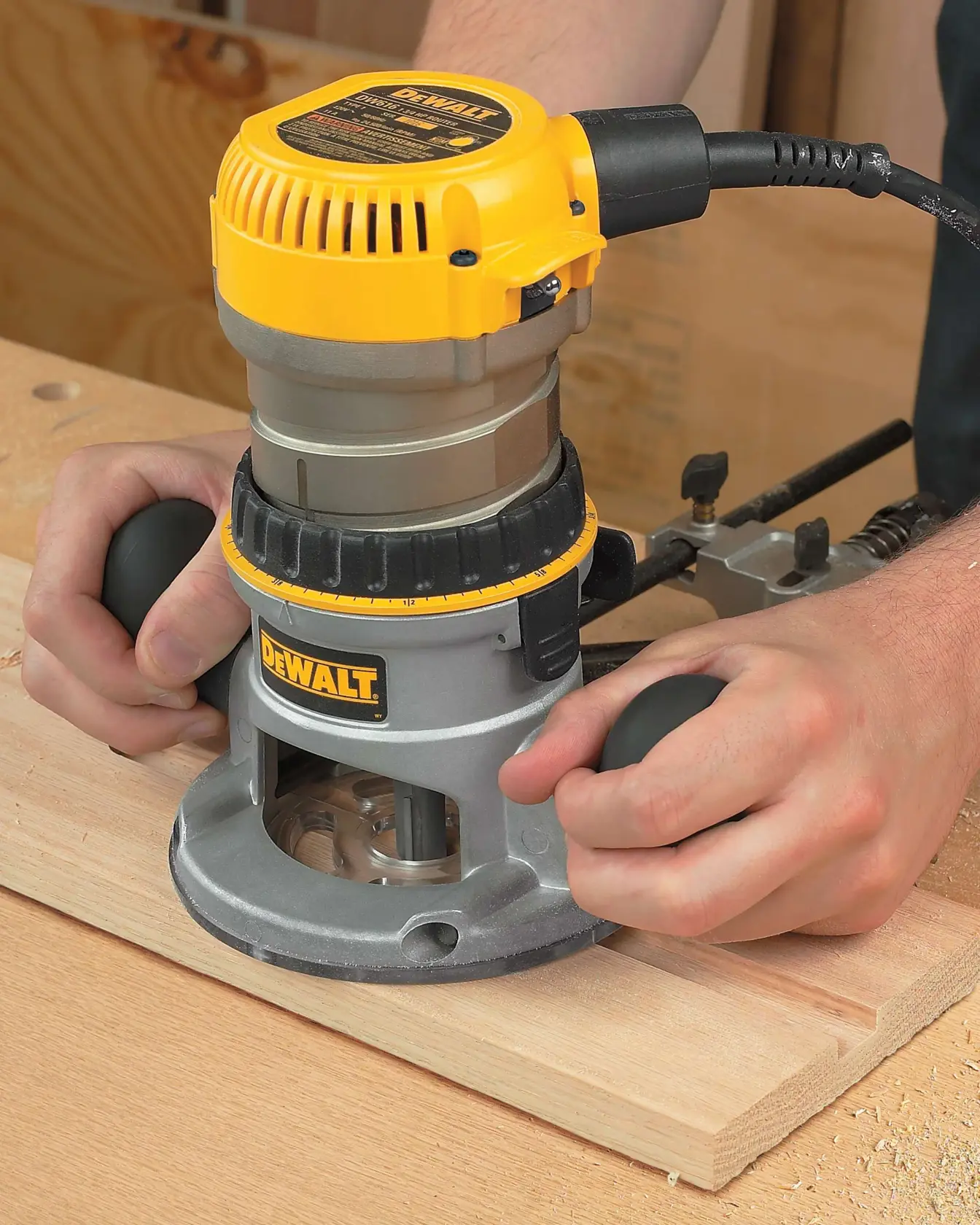 Close-up of a person operating a DEWALT electric wood router on a piece of wood, showing both hands holding the tool.