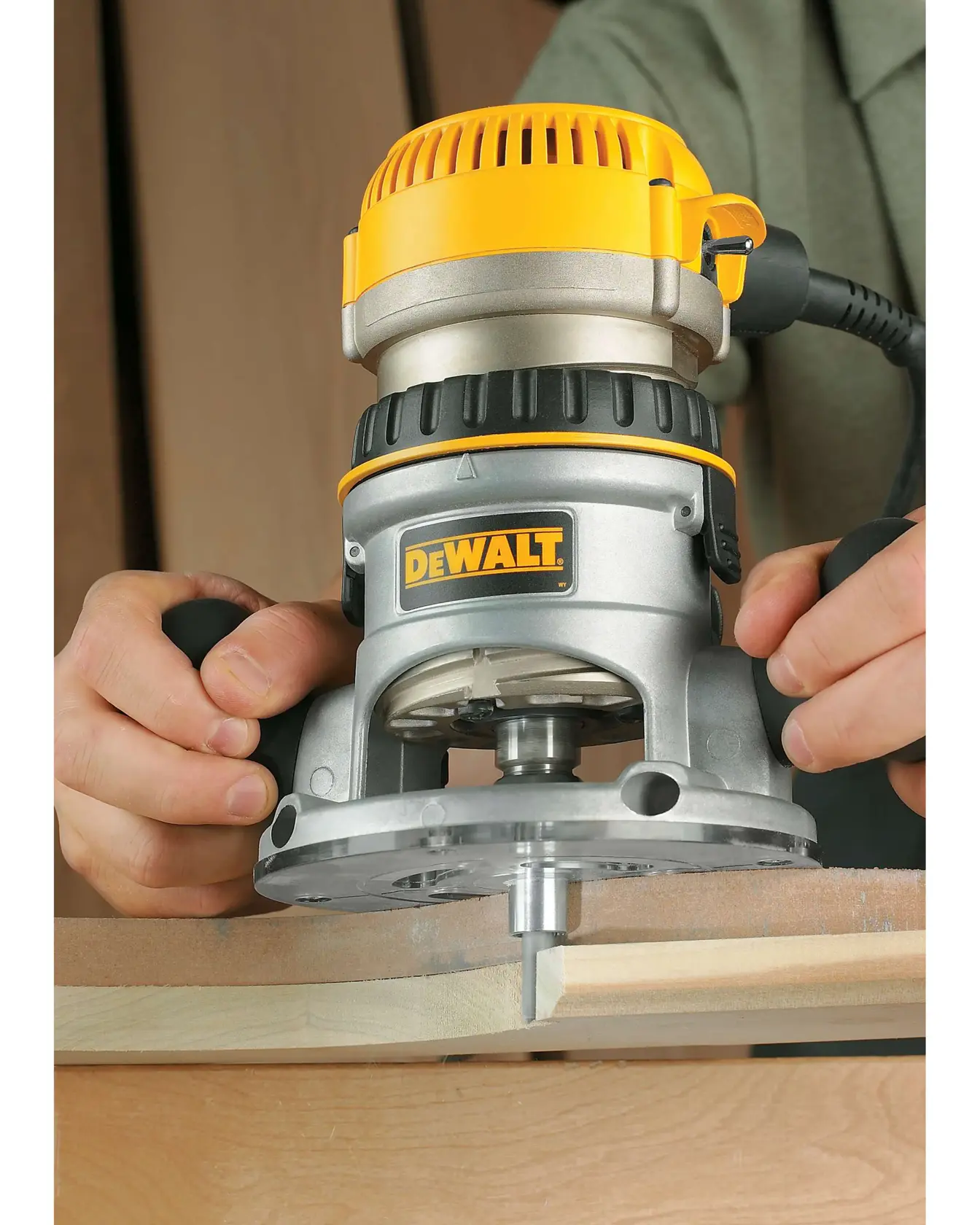 A close-up view of a DEWALT DW616 wood router being used to shape the edge of a piece of wood. The hands of a person are holding the tool, and the DEWALT logo is visible on the router body.