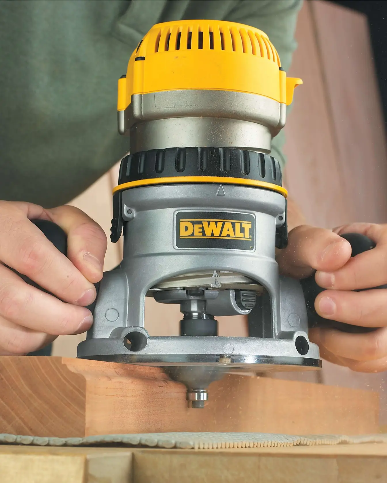 A DEWALT DW618 wood router being used by a person to shape the edge of a wooden board.