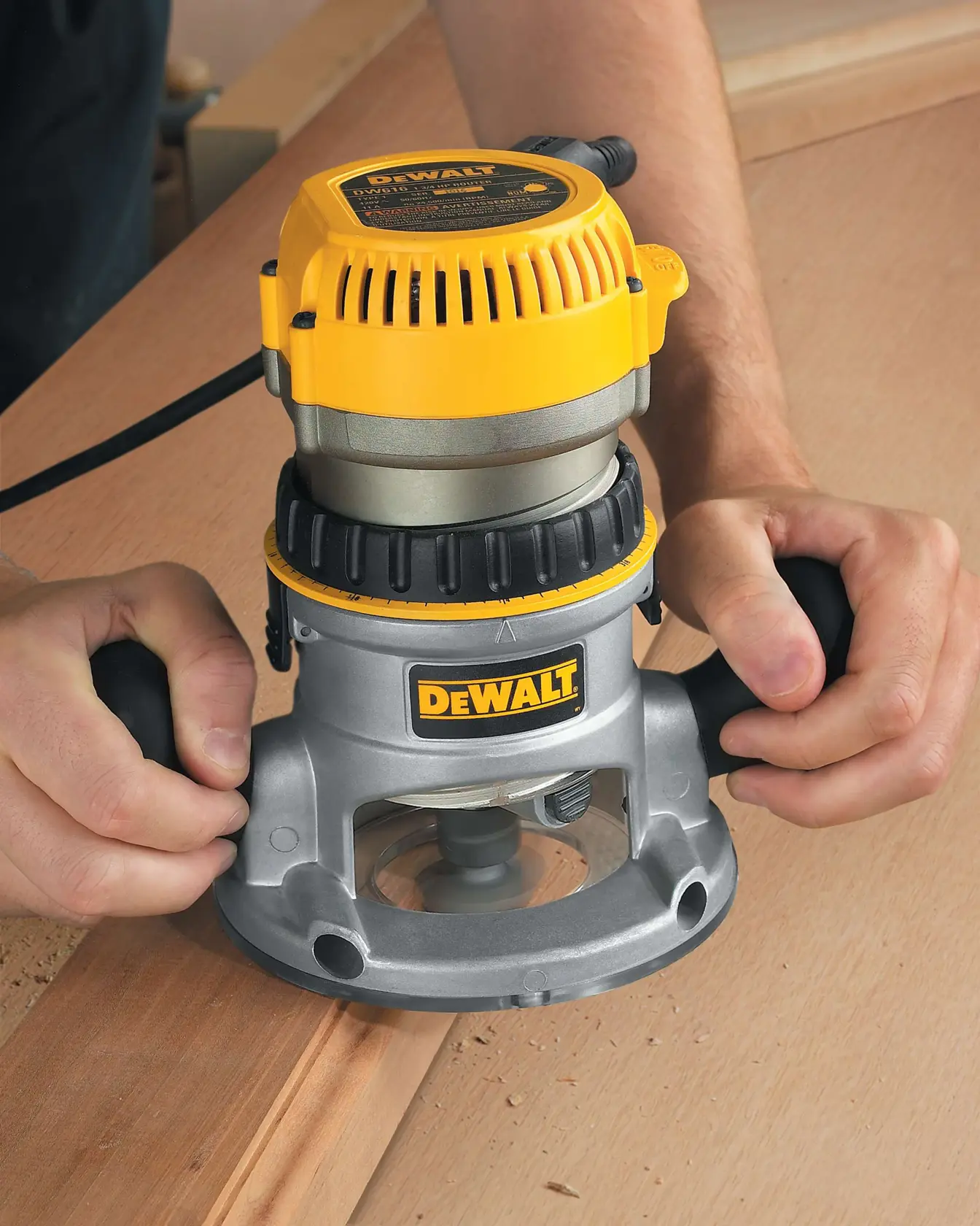 A person using a DEWALT DW618 wood router to cut or shape the edge of a wooden board.