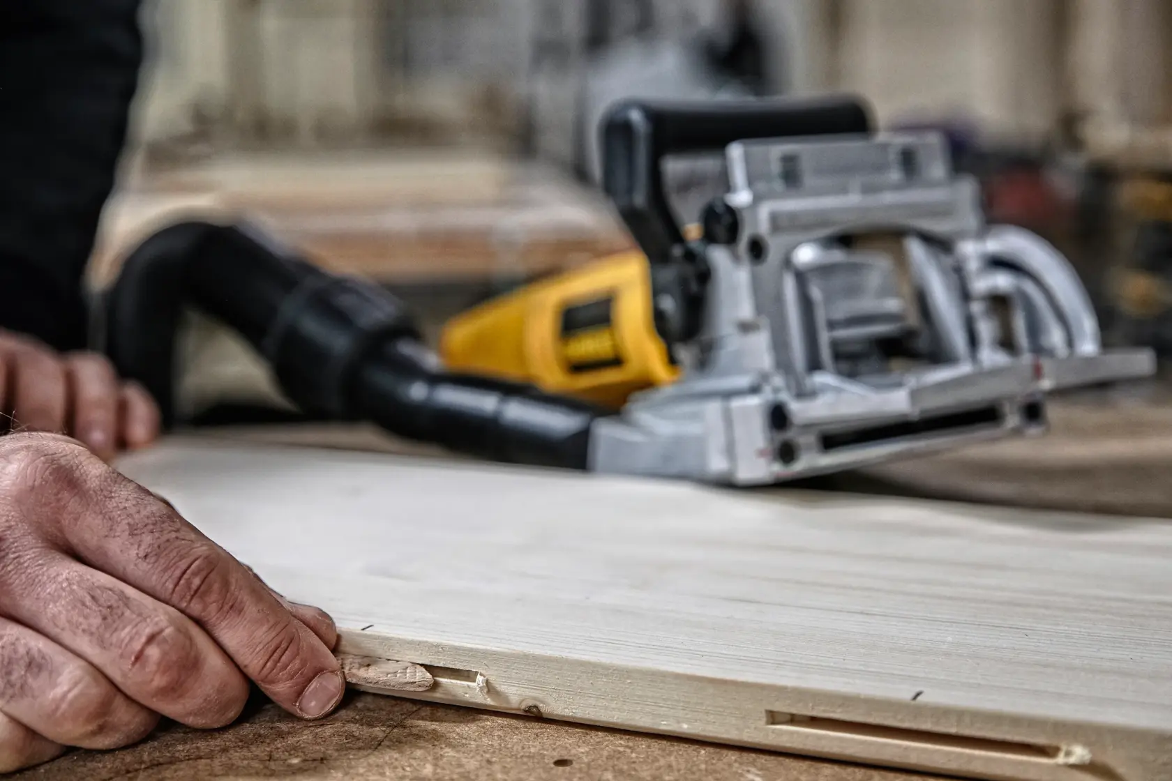 A close-up of a DEWALT biscuit joiner tool on a woodworking table, with a person inserting a wooden biscuit into a slot in a piece of wood.