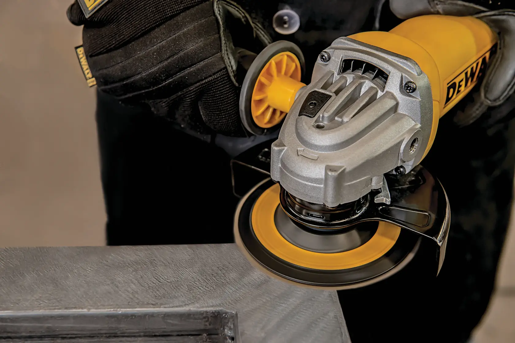 A close-up view of a person wearing black gloves using a yellow DEWALT angle grinder to smooth or polish a metal surface.