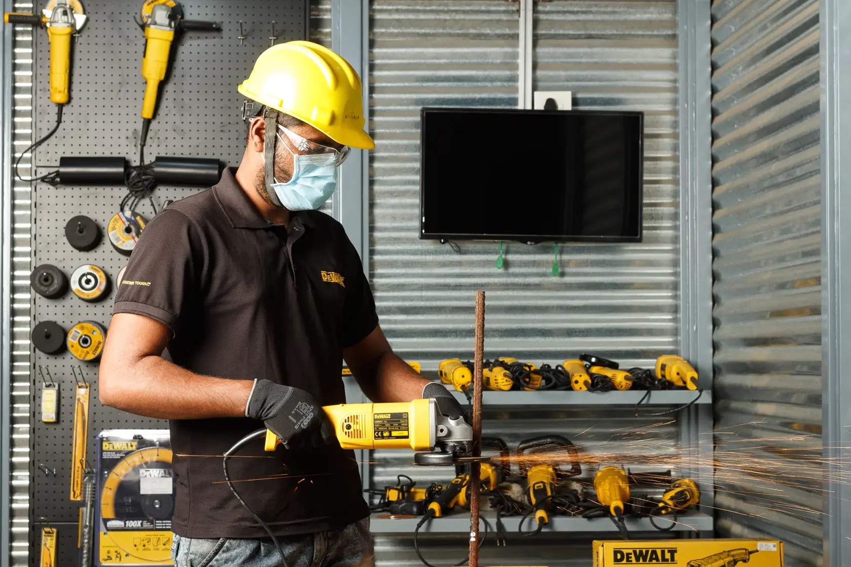 Worker uses DEWALT DW831 grinder on metal rod in workshop, wearing safety gear. Tools visible in background.