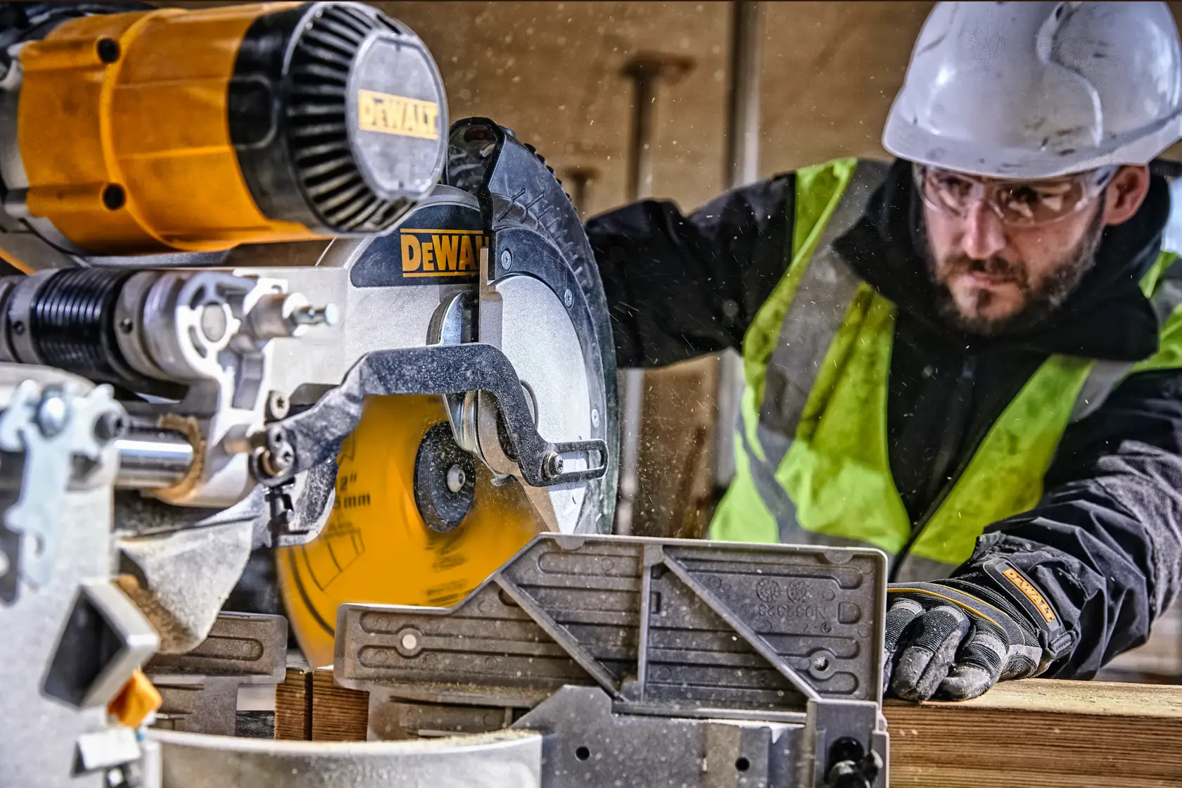 A DEWALT circular saw is in use on a construction site, cutting wood. A person wearing a safety helmet, green reflective vest, and protective gloves is operating the saw. The face of the operator is obscured for privacy.