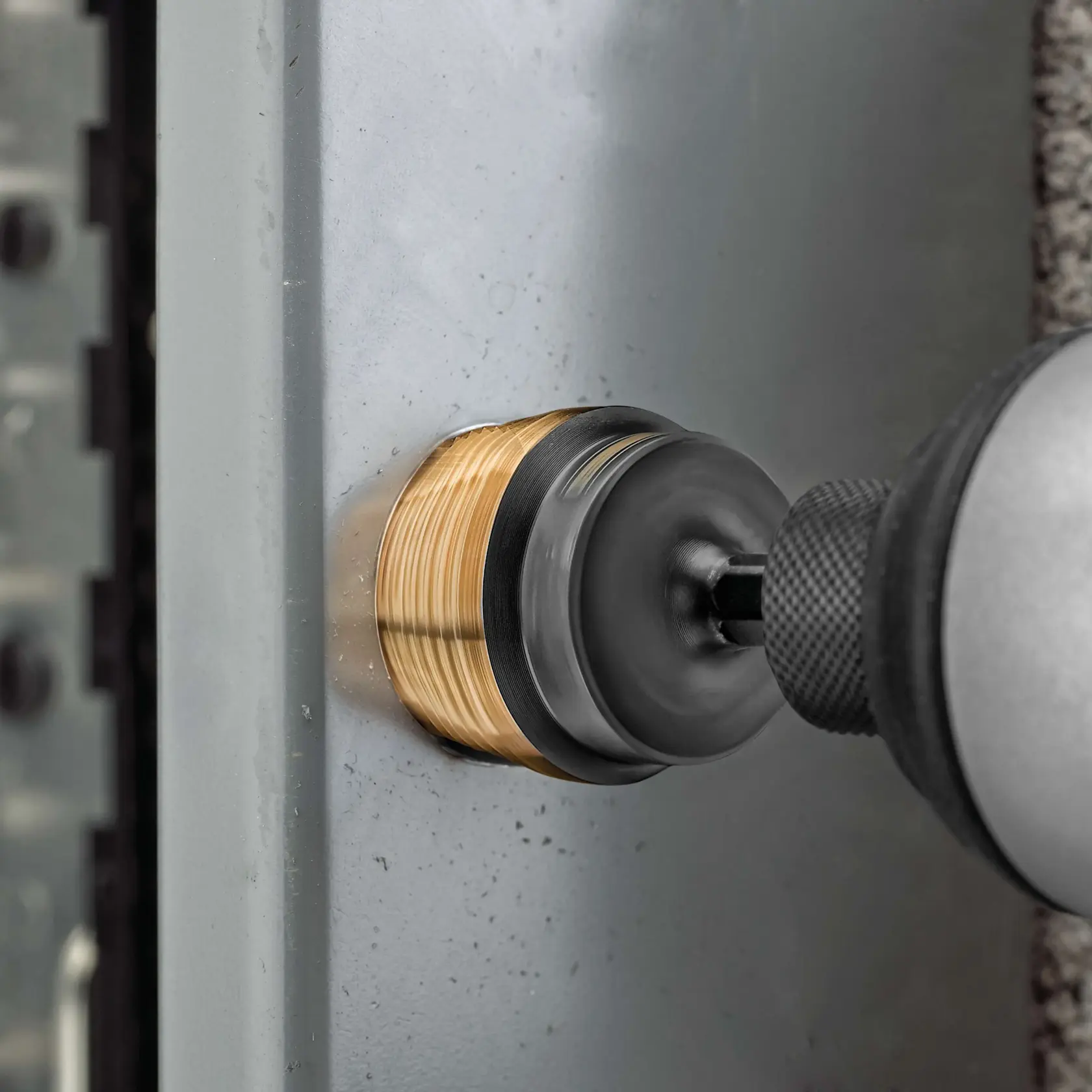 A close-up view of a drill equipped with a hole saw attachment cutting through a metal surface.