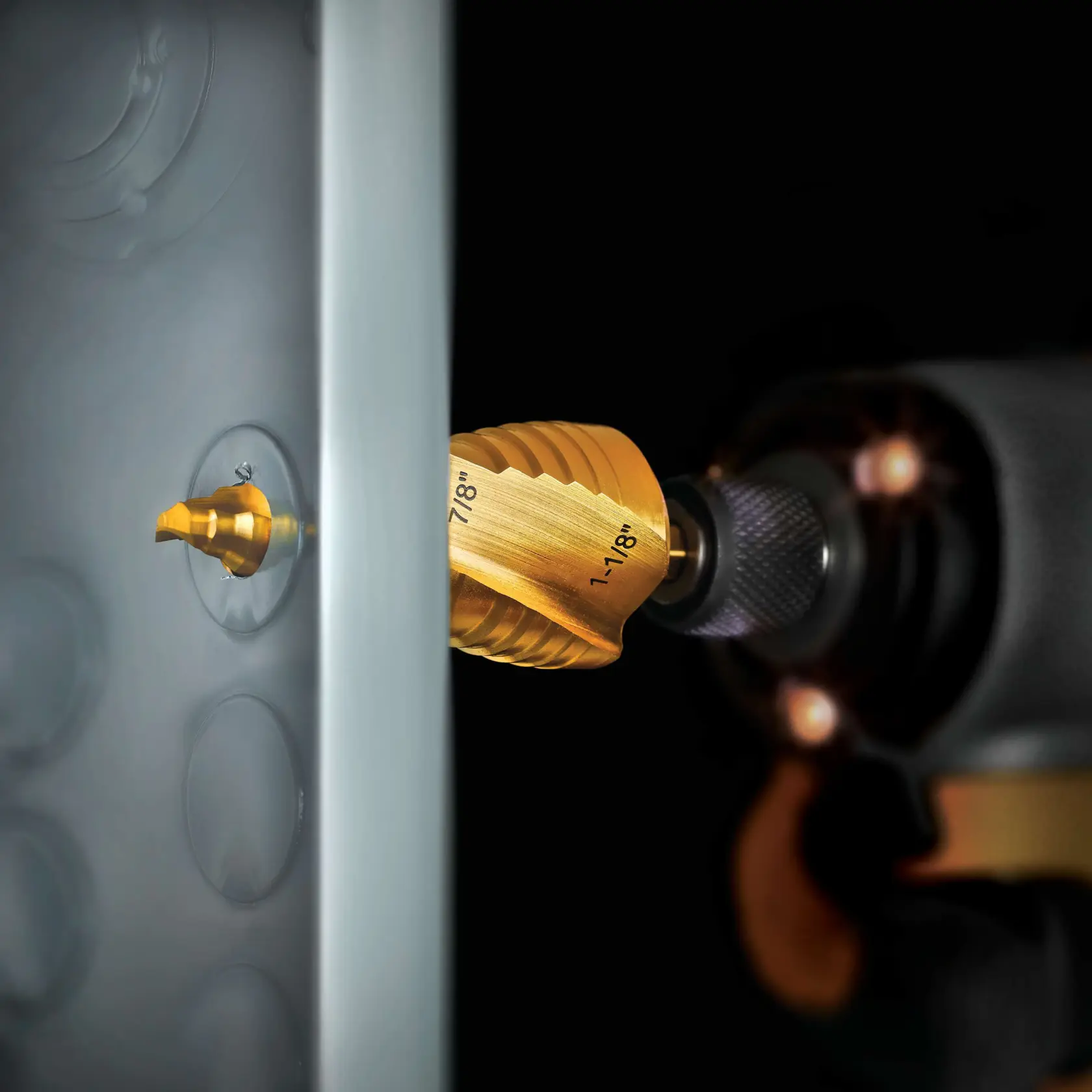 A close-up image of a gold-colored DEWALT step drill bit attached to a power drill, drilling through a metal sheet. The step drill bit has size markings visible, including 7/8" and 1-1/8".