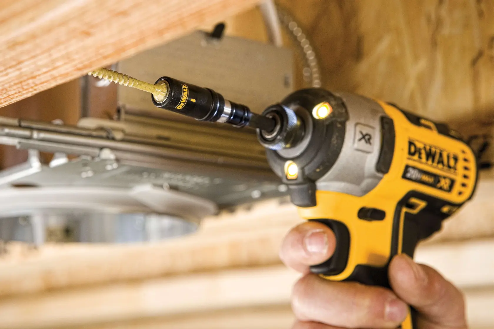 A close-up image of a hand using a yellow DEWALT cordless power drill with a screw bit attachment to fasten a screw into a piece of wood.