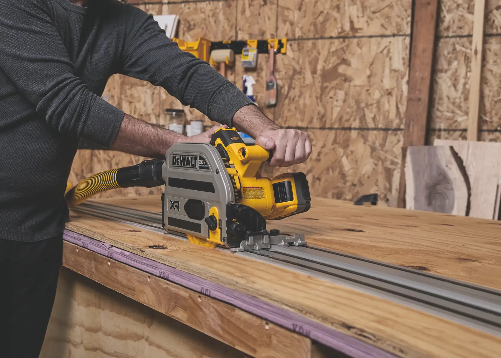 Personne utilisant une scie sur rail DEWALT pour couper du bois sur un établi dans un atelier.