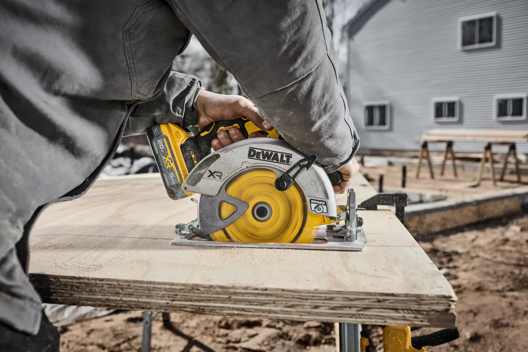 A person using a DEWALT cordless circular saw to cut a wooden board at an outdoor construction site.