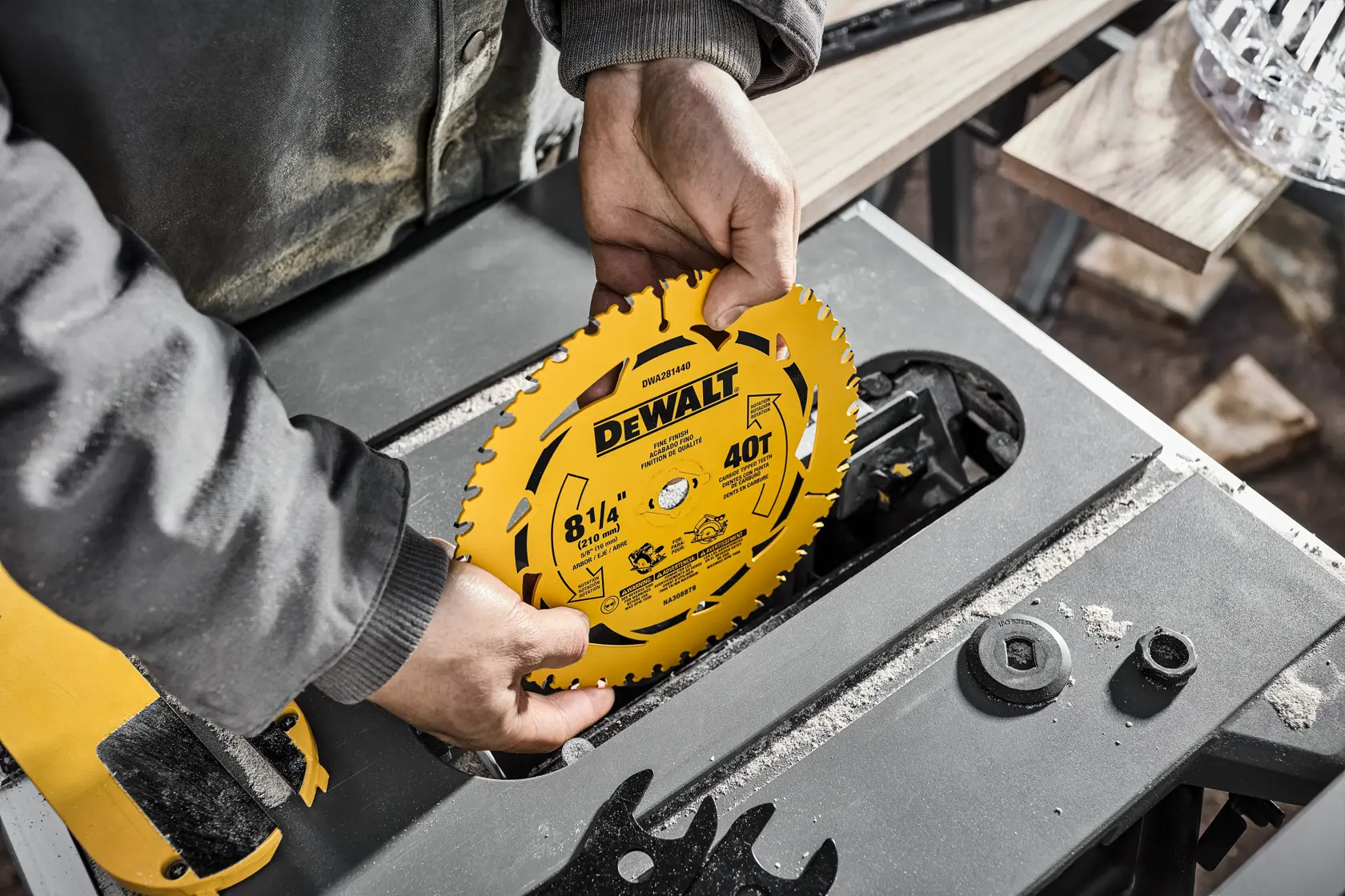A person installing a yellow DEWALT 8-1/4 inch, 40 tooth circular saw blade into a table saw, with wood and tools visible nearby.