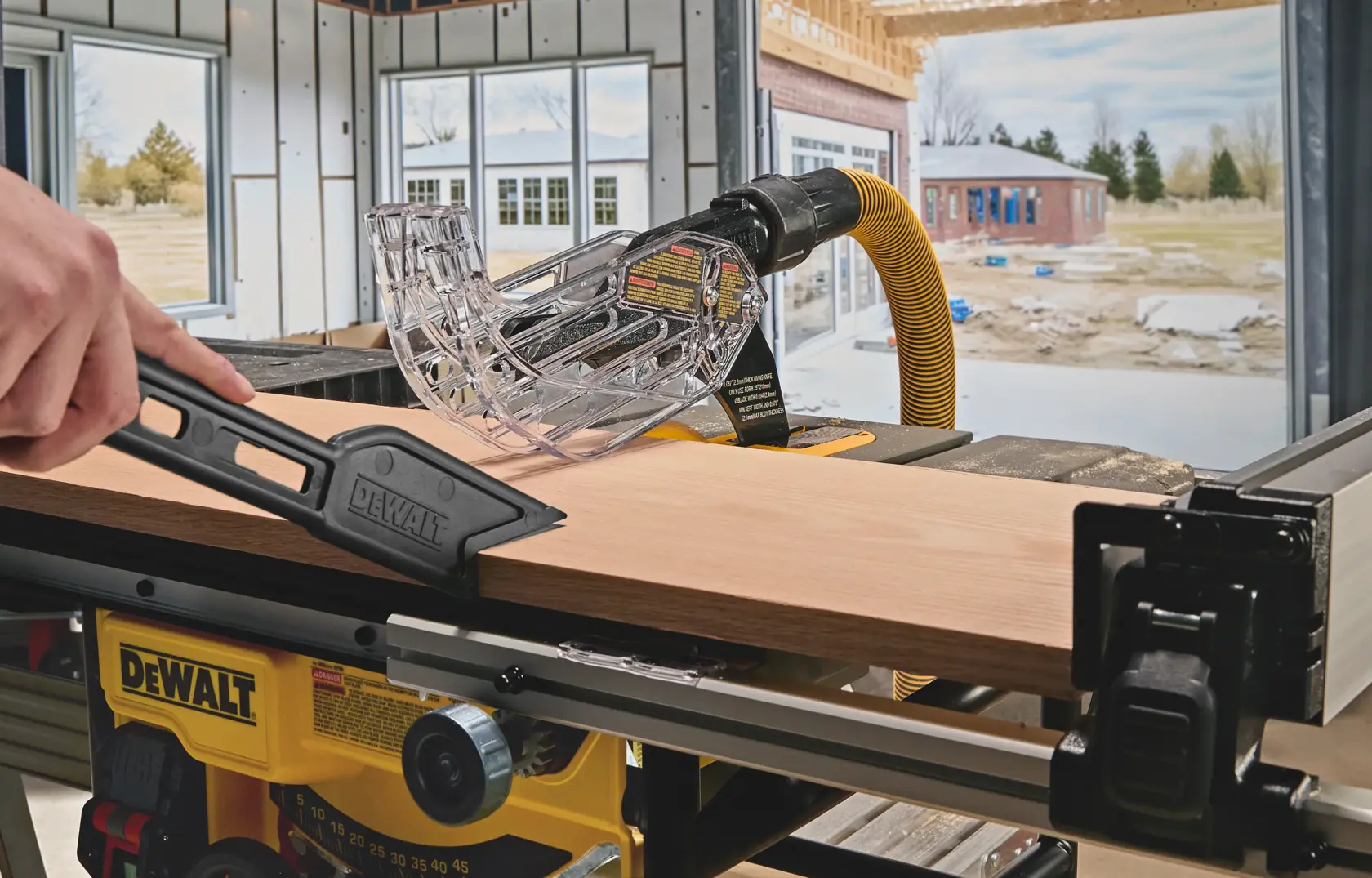 DEWALT table saw cutting wood in workshop with safety guard and push stick in use.
