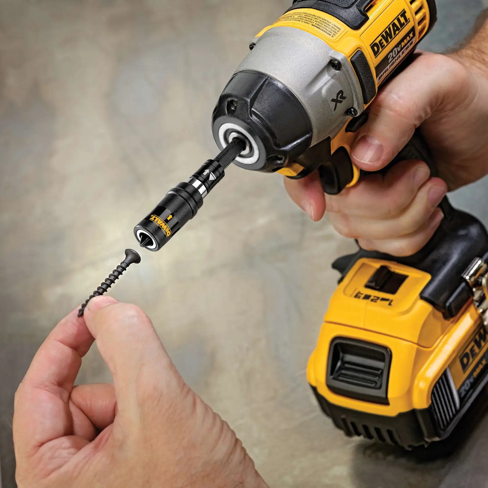 A close-up view of a person holding a DEWALT cordless drill equipped with a black magnetic screw holder attachment, positioning a screw into the holder.