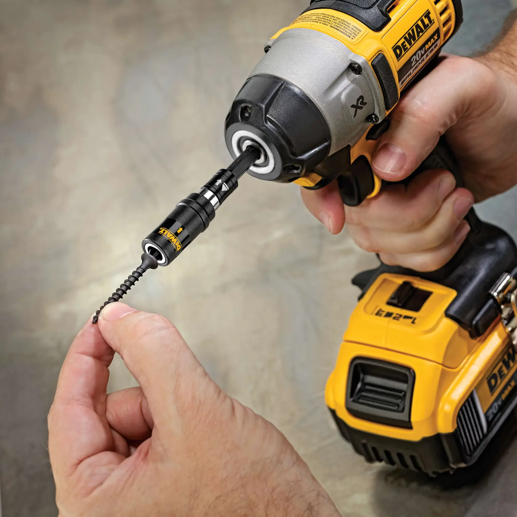 A close-up image of a DEWALT cordless power drill with a screw-holding bit attached. A hand is holding a screw near the tip of the bit, preparing for use.