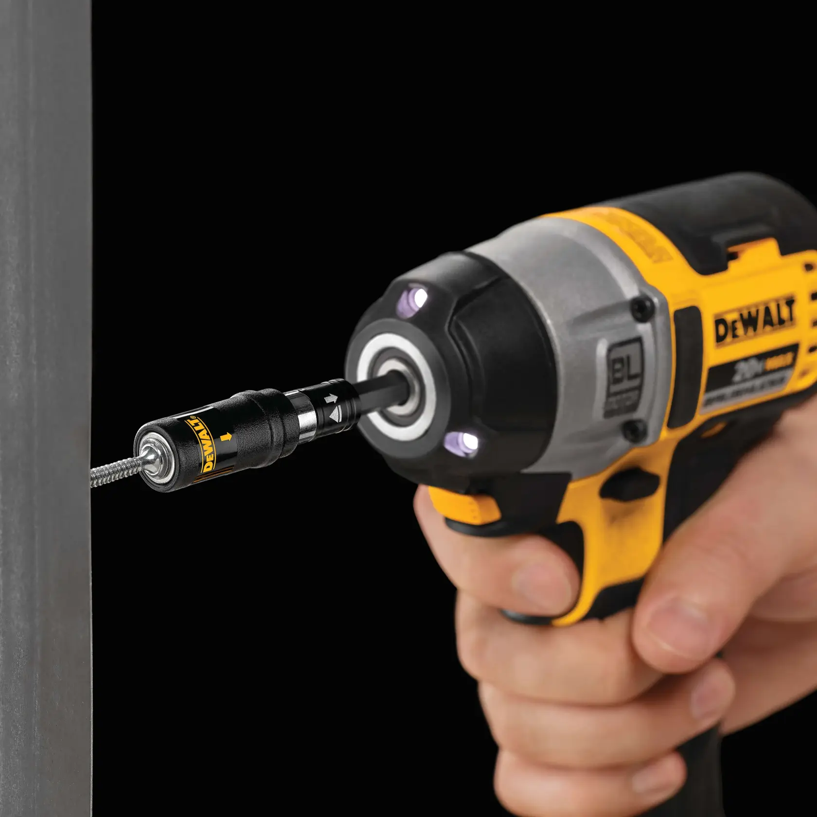 A close-up of a DEWALT impact driver being used to drive a screw into a metal surface. The tool features a bit holder attachment and LED lights around the chuck.