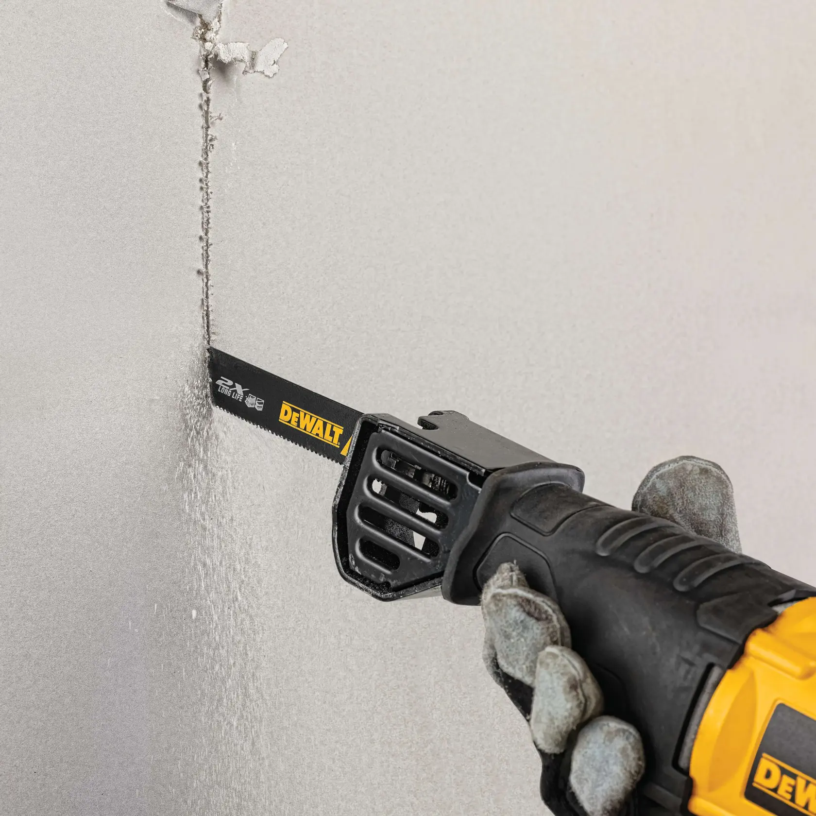 A person wearing gloves is using a DEWALT reciprocating saw to cut a vertical line through a drywall surface.