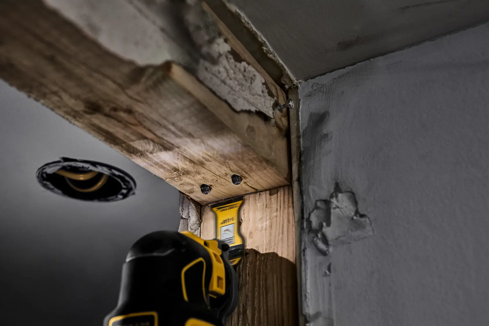 A DEWALT oscillating tool is being used to cut or sand a piece of wood near a wall corner during construction or renovation.