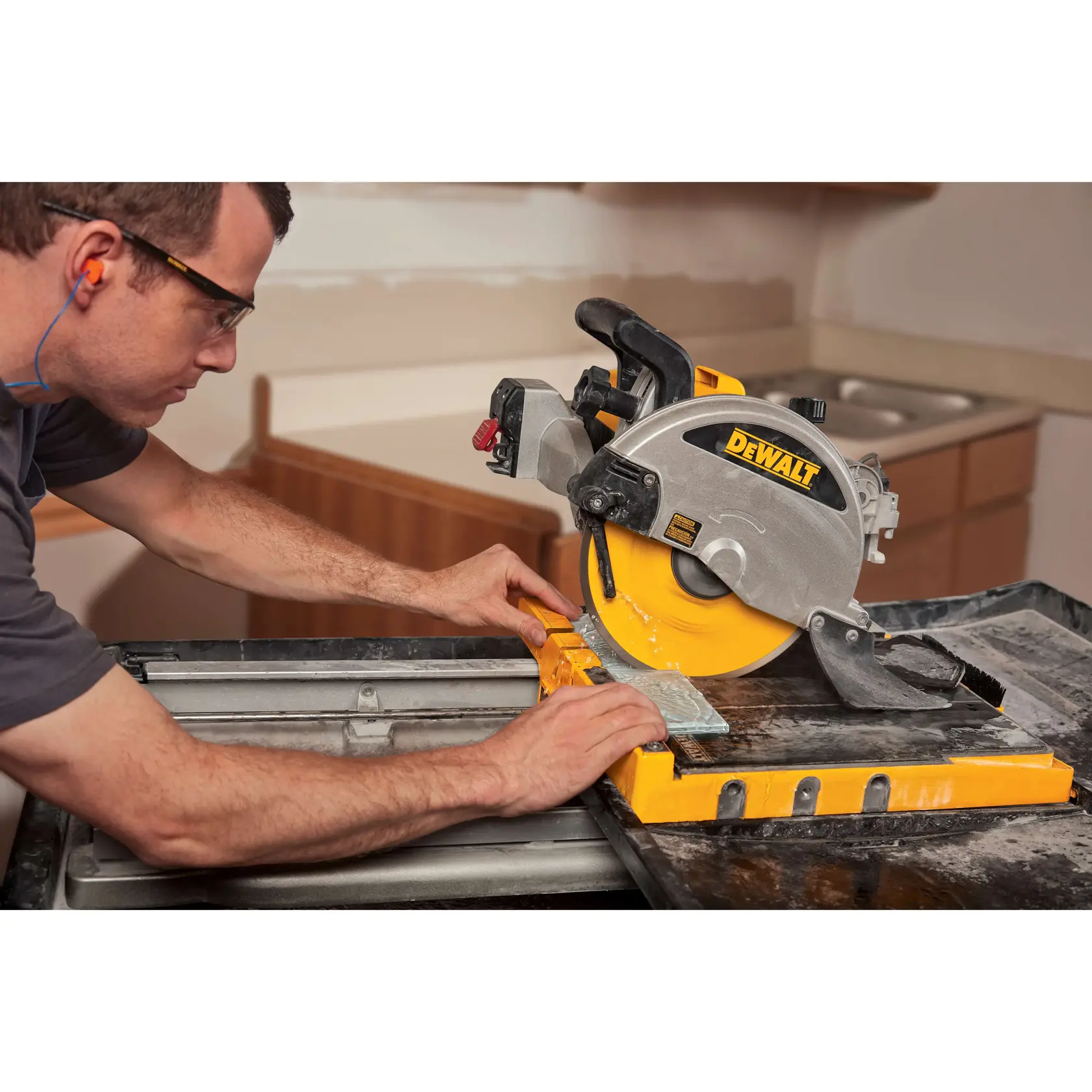 A person using a DEWALT tile saw to cut a piece of tile in an indoor workspace. The saw features a yellow and silver design, and the person is wearing ear protection.