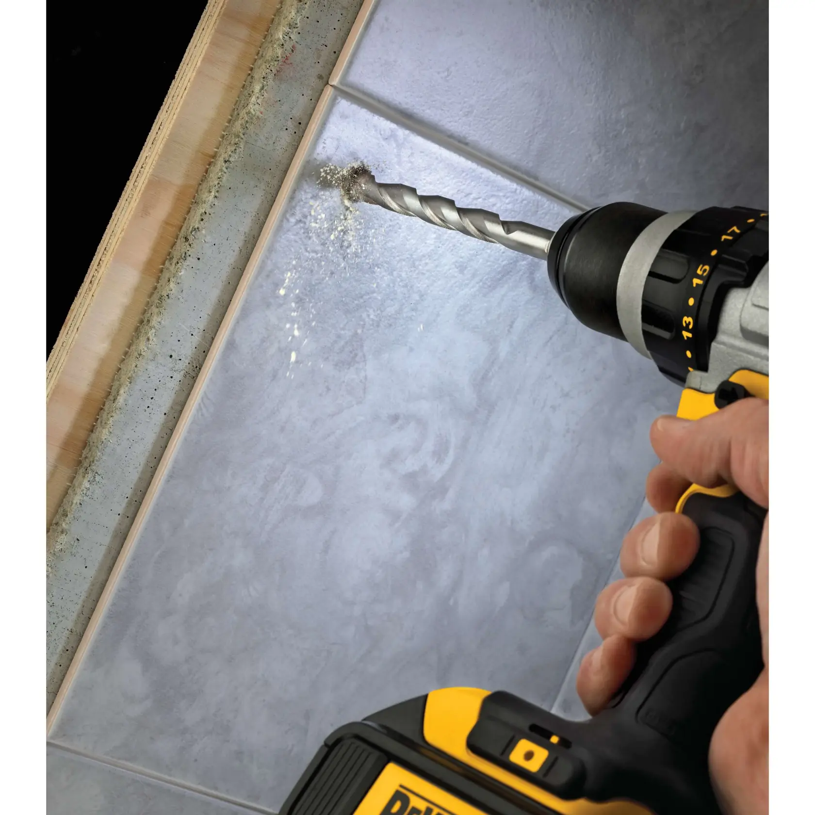 A close-up of a person using a DEWALT power drill to drill into a tiled surface, with dust and debris visible.