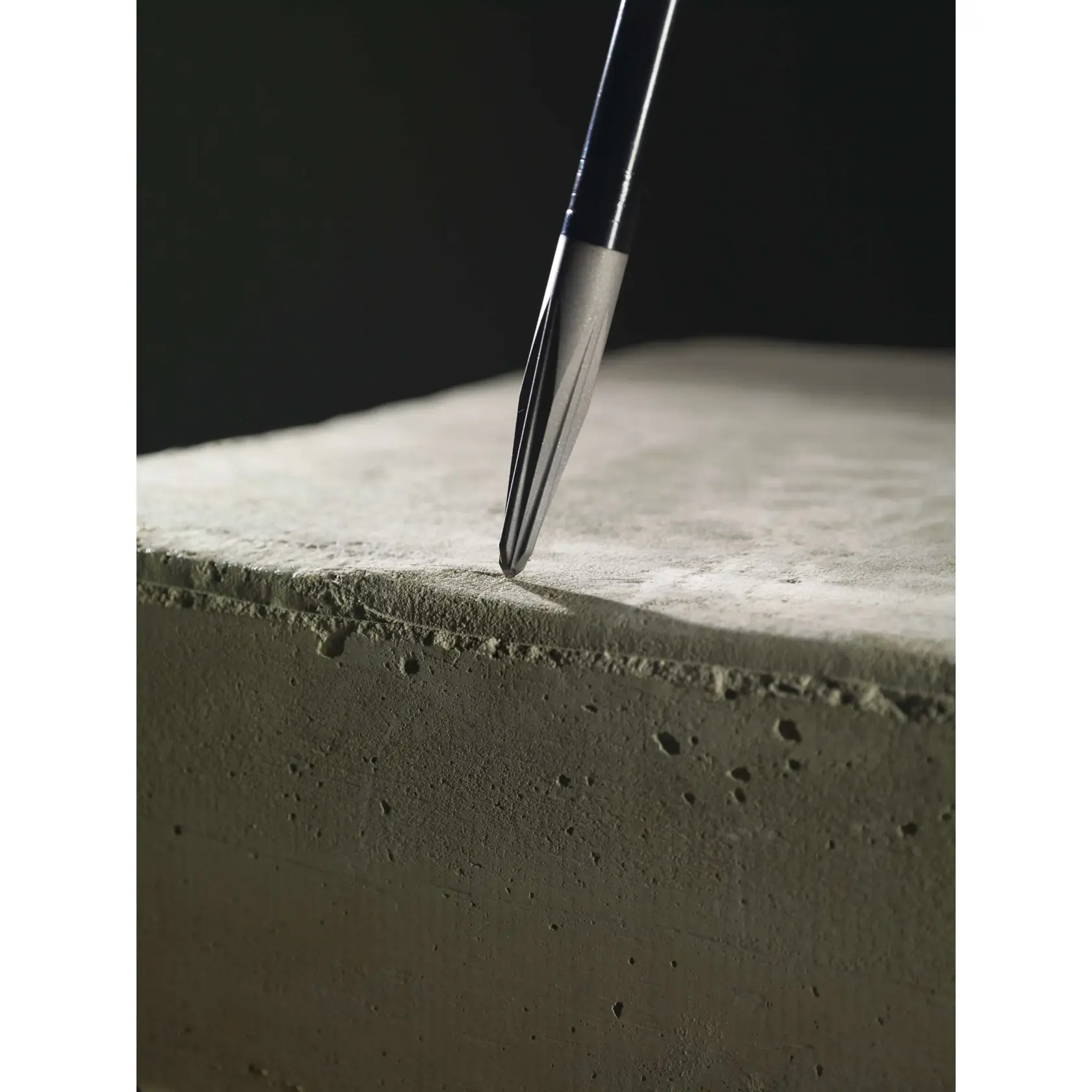 Close-up of a drill bit positioned on the surface of a concrete block, highlighting its pointed tip and fluted design.