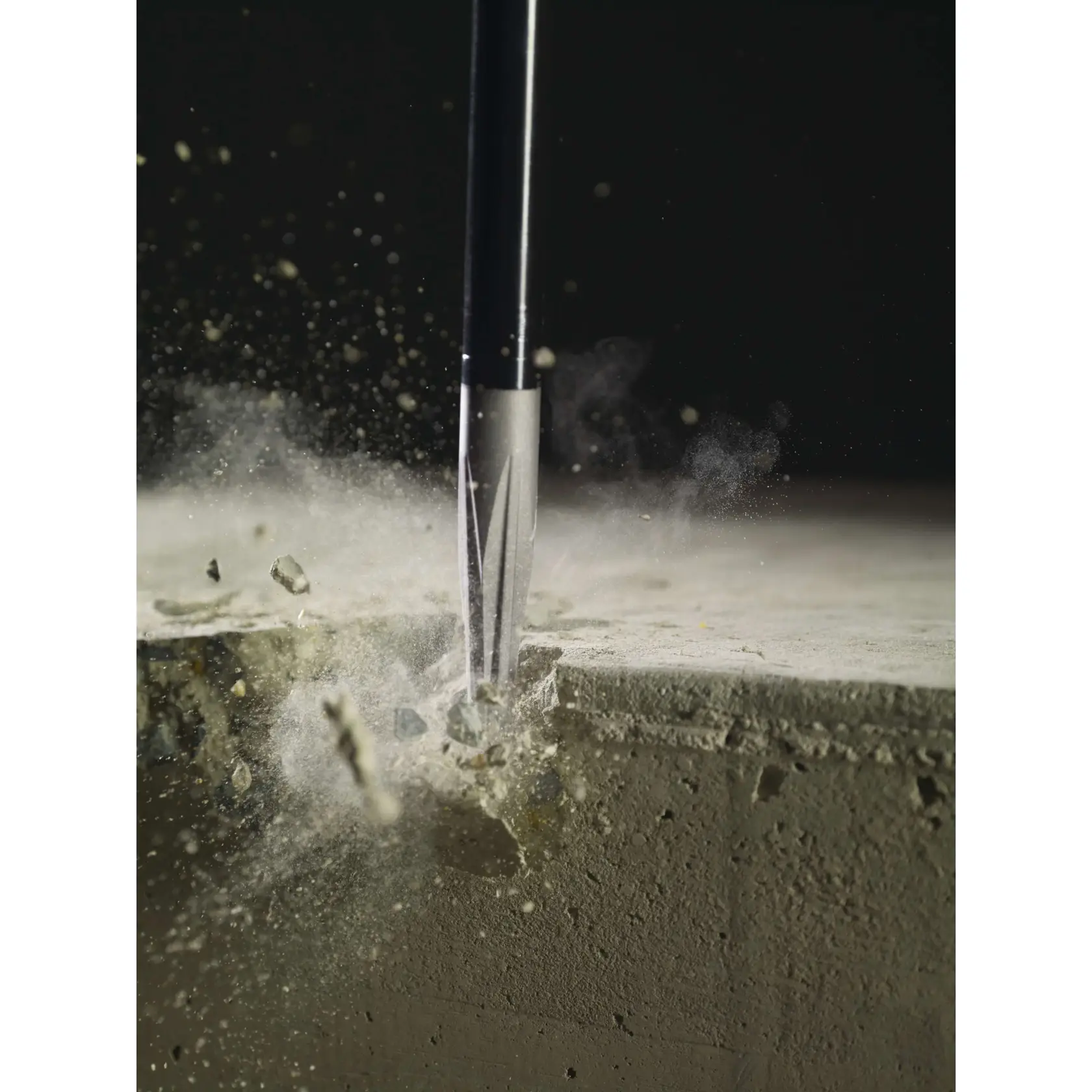 Close-up image of a chisel bit breaking through a concrete surface, with dust and small debris flying.