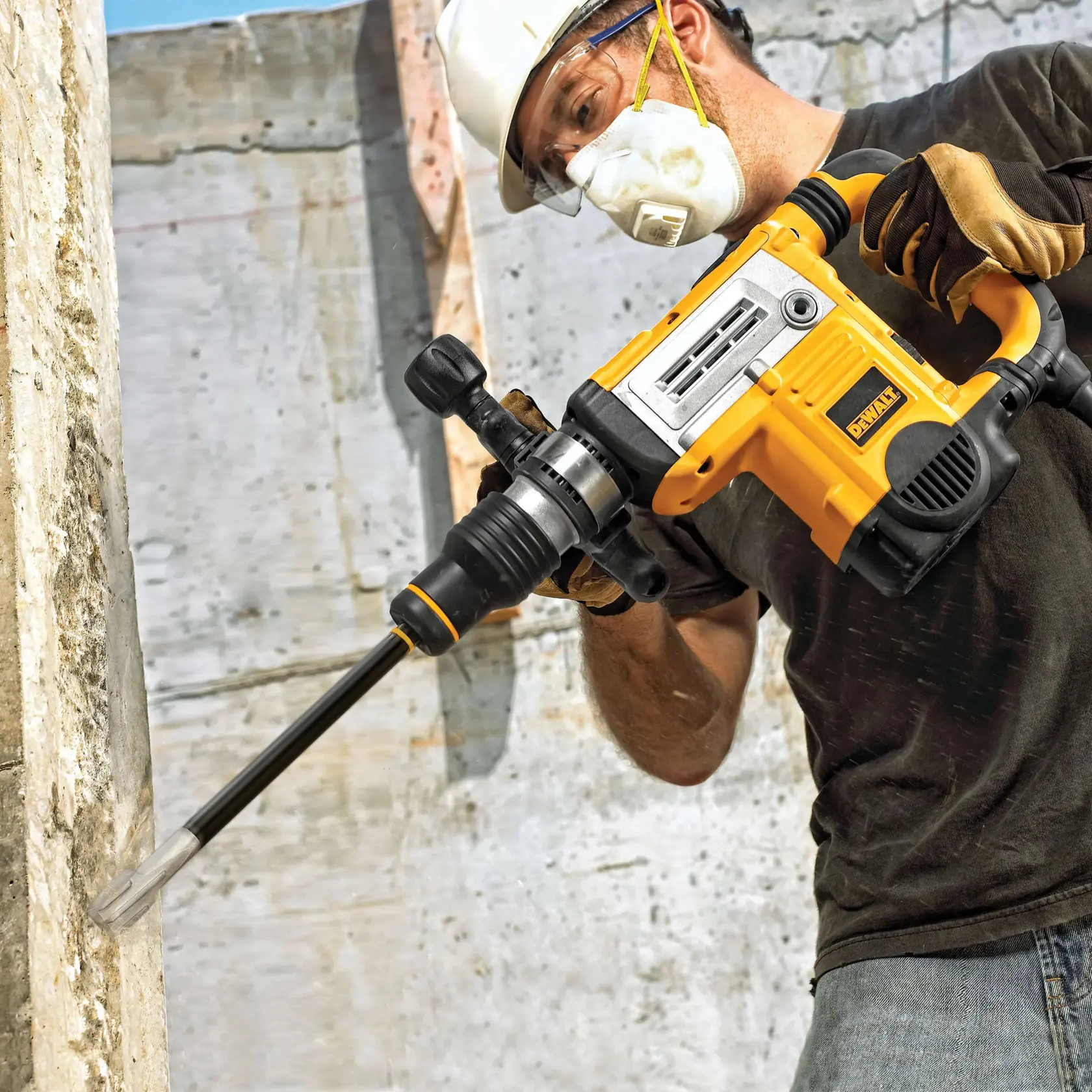 A person wearing work gloves and a safety helmet using a DEWALT rotary hammer drill (SKU: DWA5852) to drill into a concrete wall at a construction site.