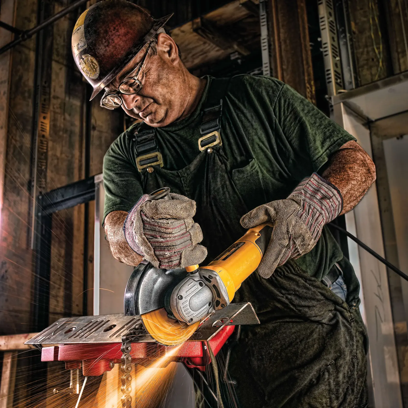 A person wearing work gloves and a hard hat is using a DEWALT angle grinder to cut metal, producing sparks, in an industrial setting.
