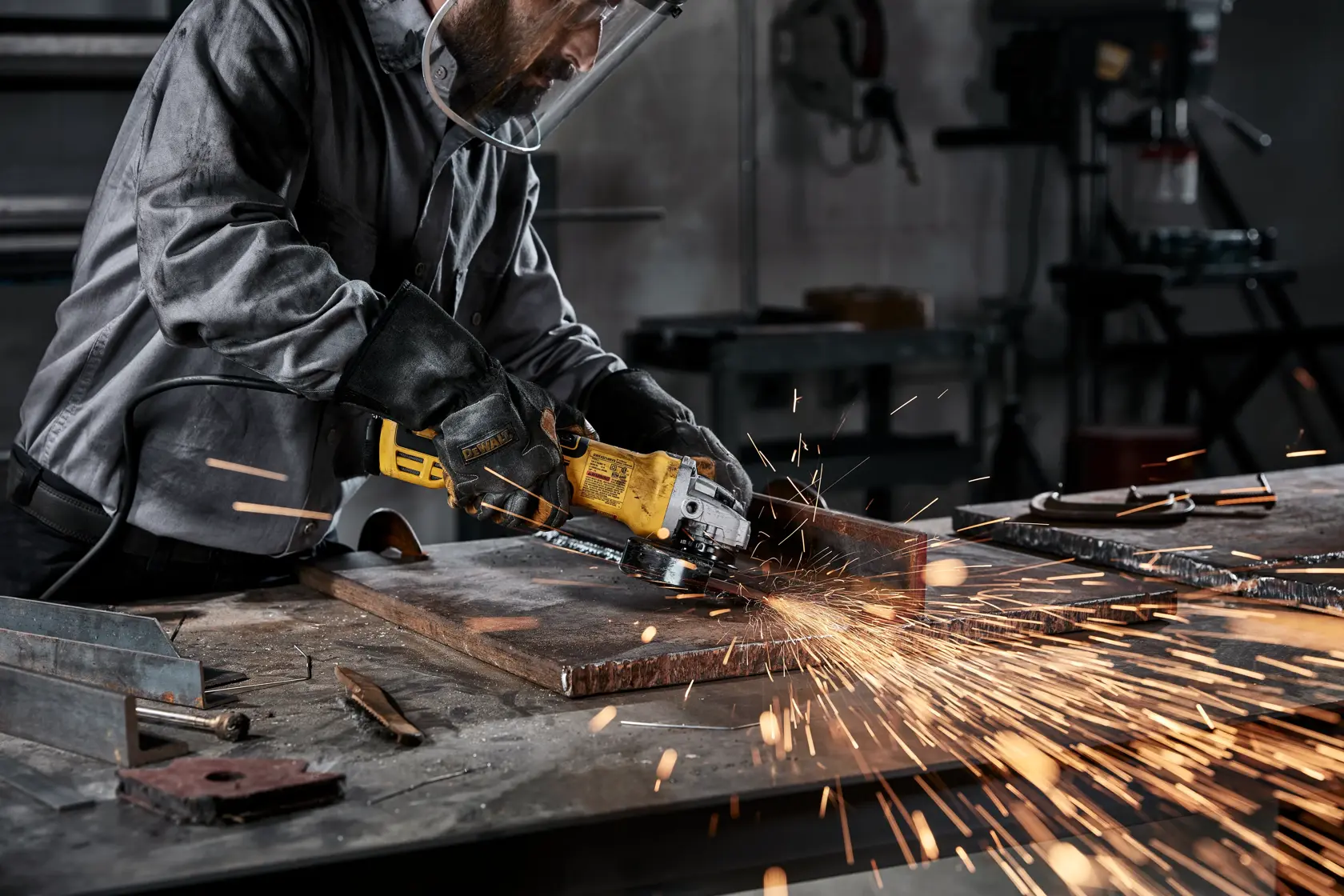 Person wearing protective gear using a yellow DEWALT angle grinder to cut metal on a workbench, creating sparks in a workshop setting.