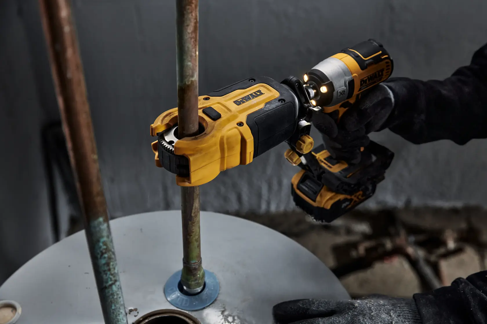 A DEWALT power tool being used to cut or work on a metal pipe attached to a surface. The worker is wearing black gloves while operating the yellow and black tool.