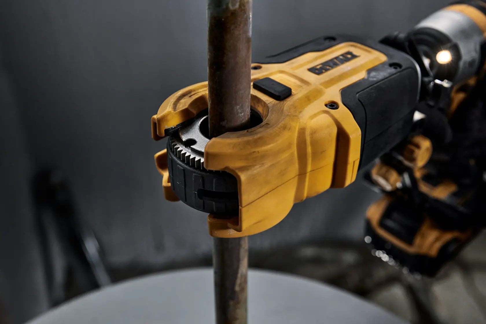 Close-up of a DEWALT power tool being used to cut or thread a metal pipe, showing the yellow and black tool gripping the pipe firmly.