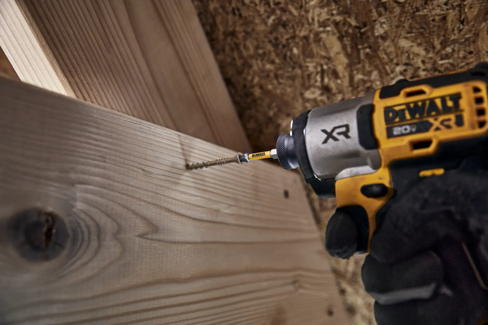A close-up of a DEWALT cordless power drill driving a screw into a piece of wood.