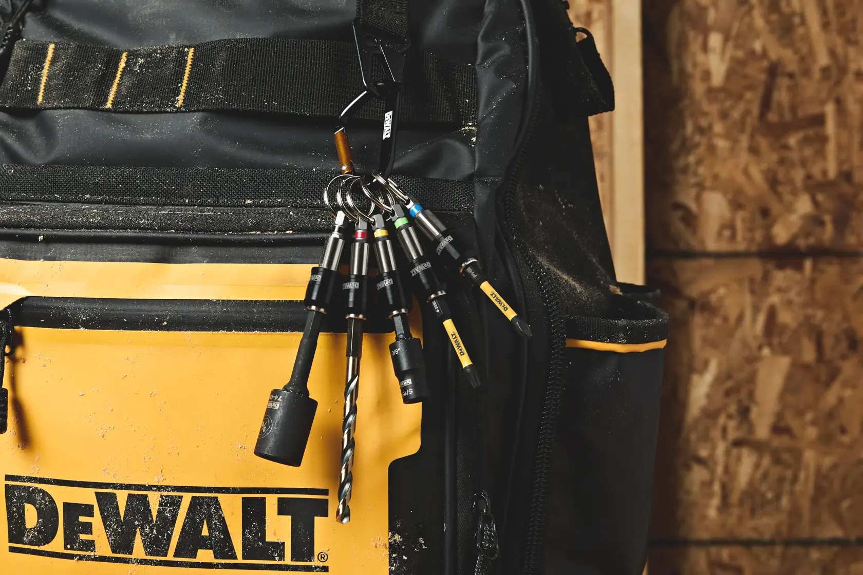 A set of DEWALT branded screwdriver bits attached to a carabiner clip, hanging from the belt loop of a person's jeans. The bits are organized with colored rings and are designed for easy access during construction or DIY work.