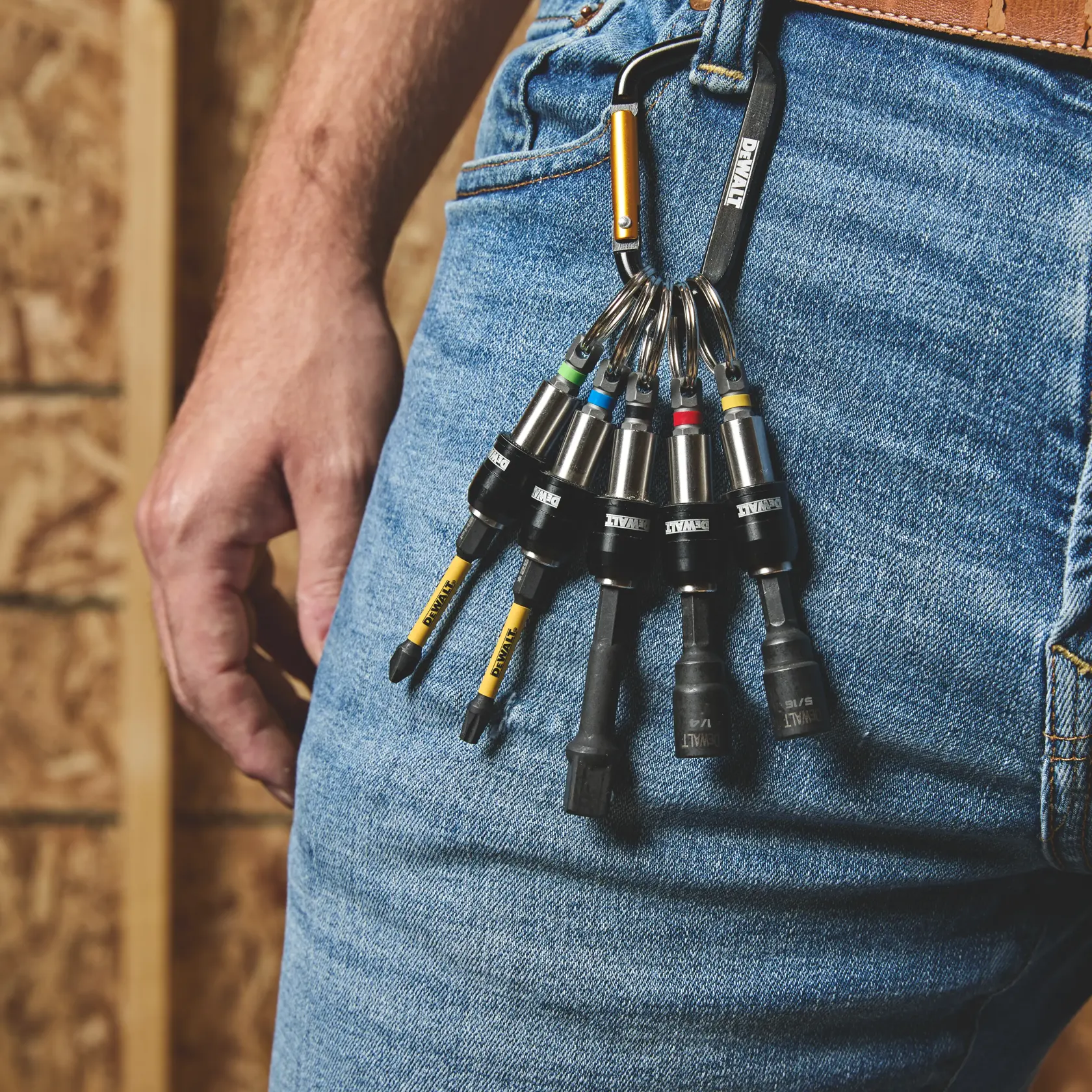 A set of DEWALT branded screwdriver bits attached to a carabiner clip, hanging from the belt loop of a person's jeans. The bits are organized with colored rings and are designed for easy access during construction or DIY work.