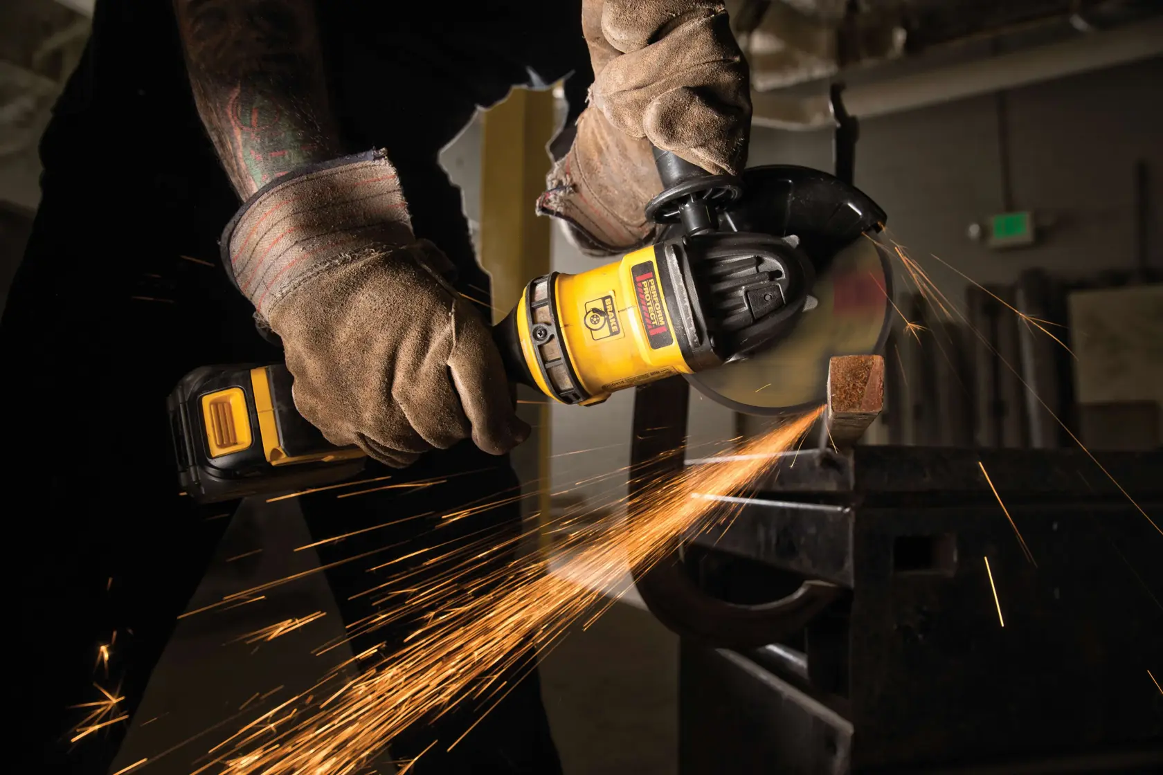 A person wearing protective gloves using a yellow DEWALT cordless angle grinder to cut through metal, with sparks flying in a workshop setting.