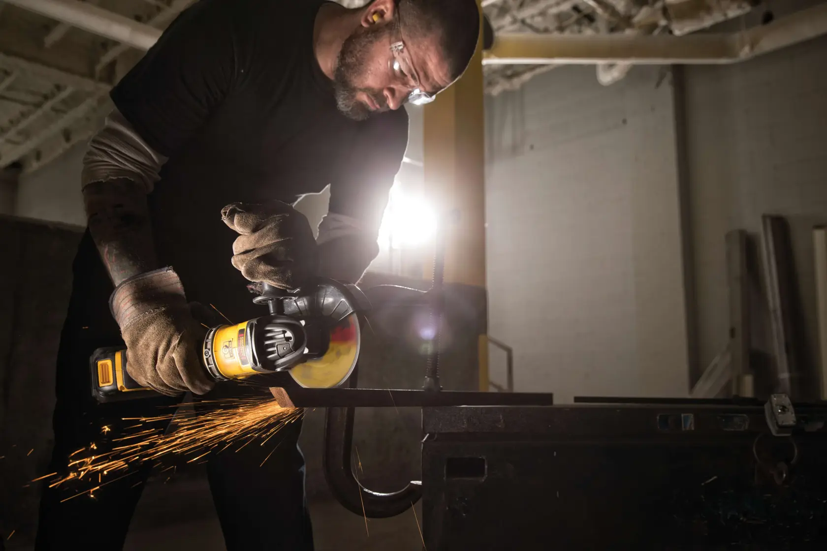 A person wearing protective gloves operates a DEWALT angle grinder, generating sparks while cutting metal in an industrial setting.