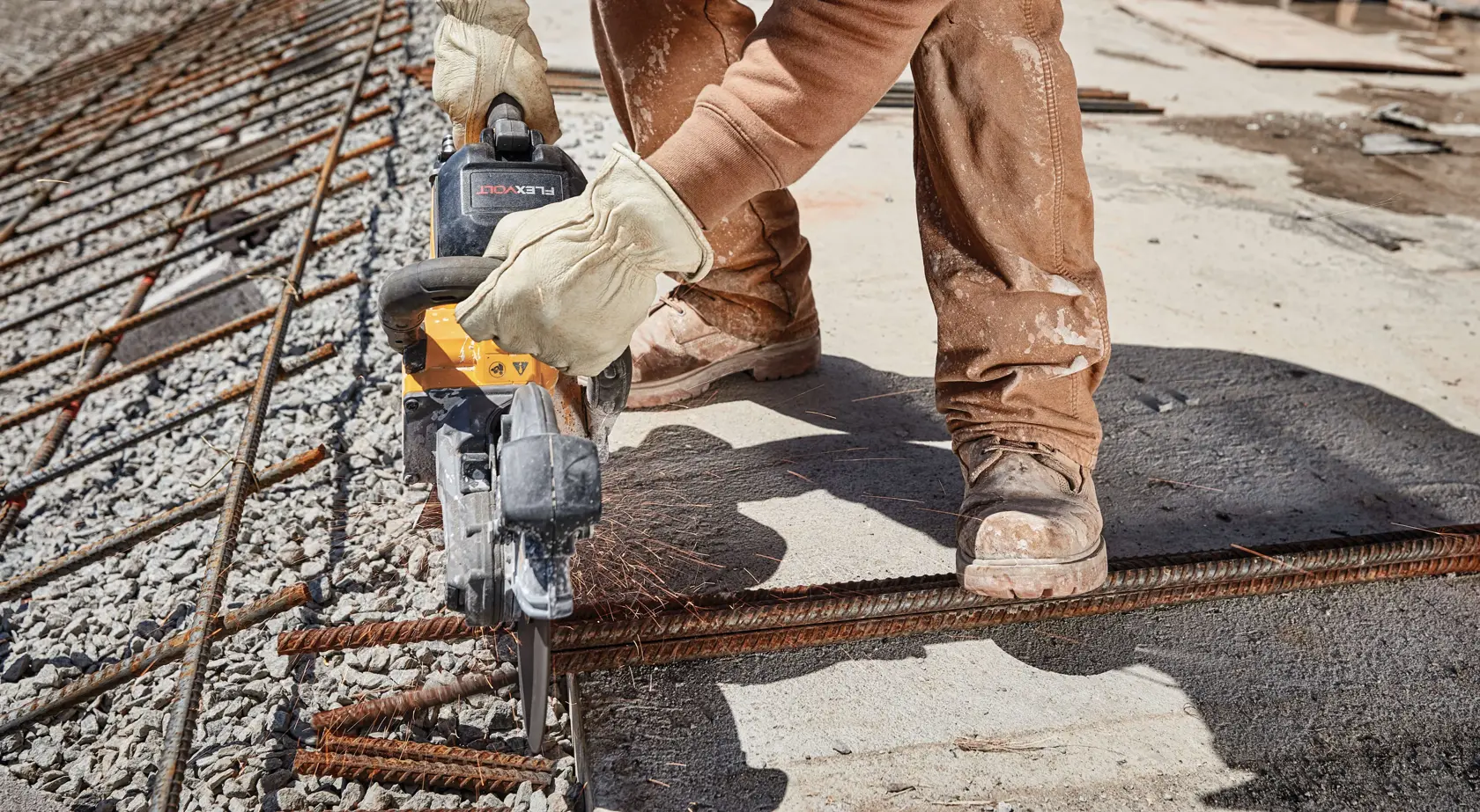 A person wearing work gloves and boots using a DEWALT power tool to cut through rebar on a construction site.