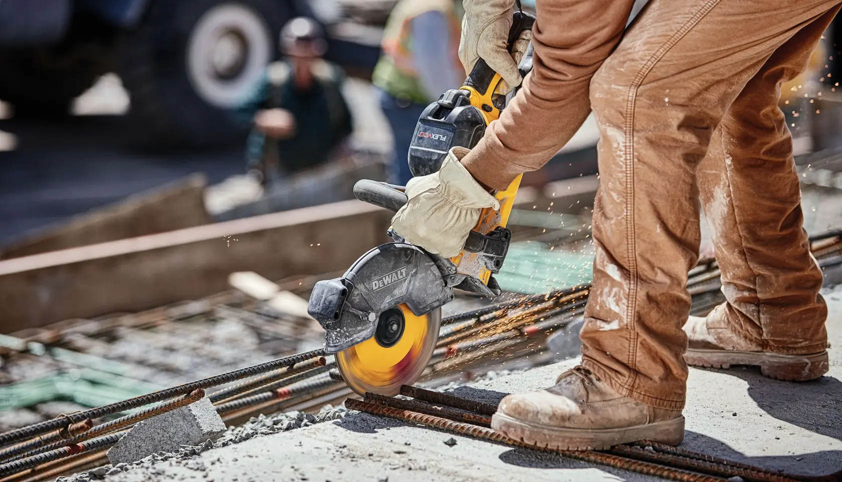 A worker using a DEWALT power cut-off saw to cut through metal rebar at a construction site. The saw is handheld and is producing sparks as it cuts. The worker is wearing gloves, brown work pants, and construction boots.