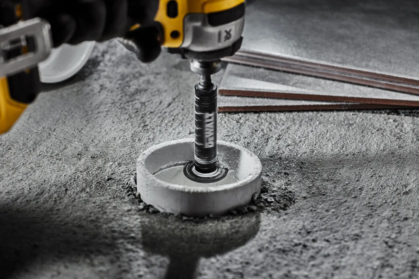 DEWALT drill with hole saw bit cutting a circular hole in concrete. Close-up tool view.