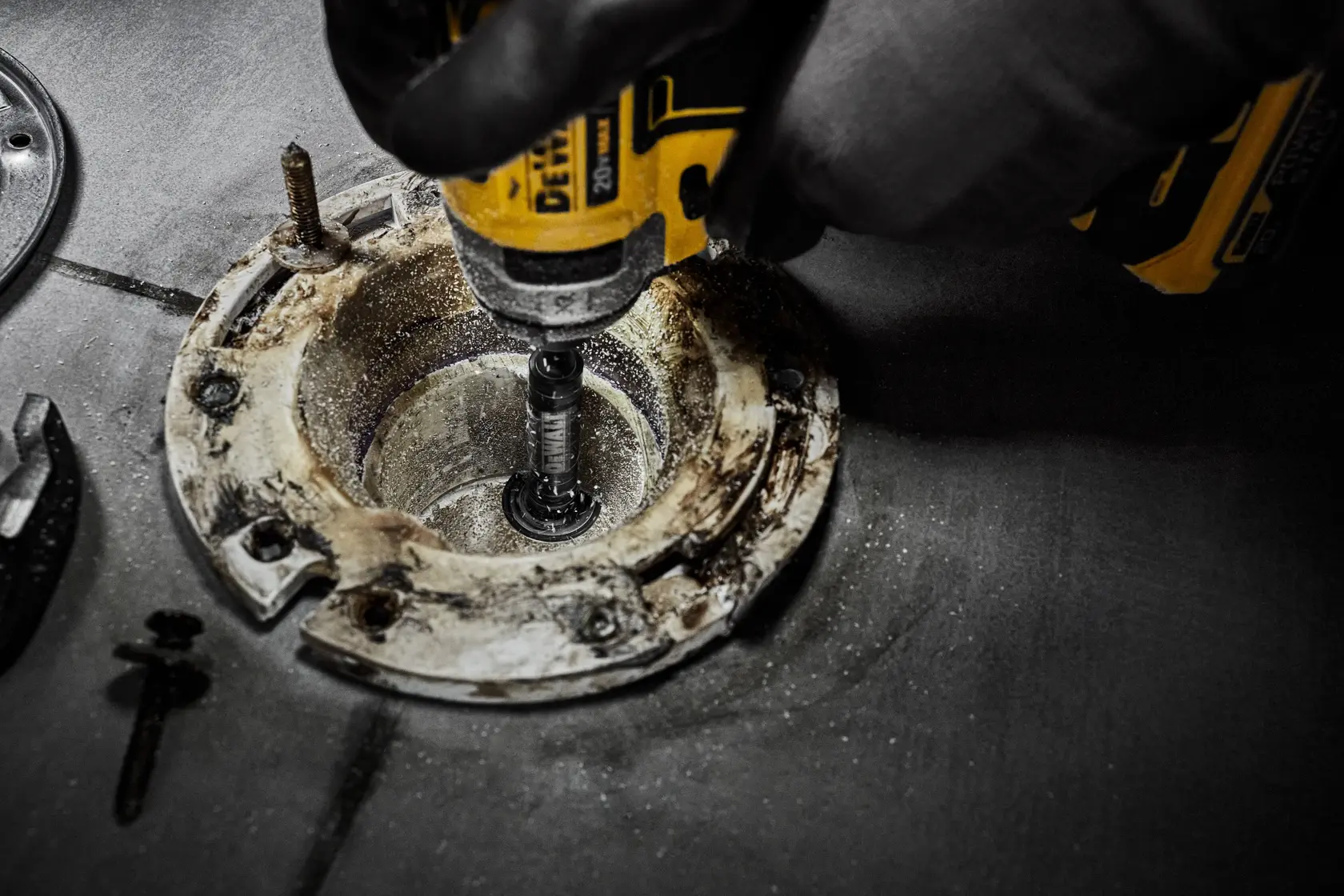 A DEWALT tool is used to drill into a metal fixture, with a gloved hand operating the device on a workshop surface.