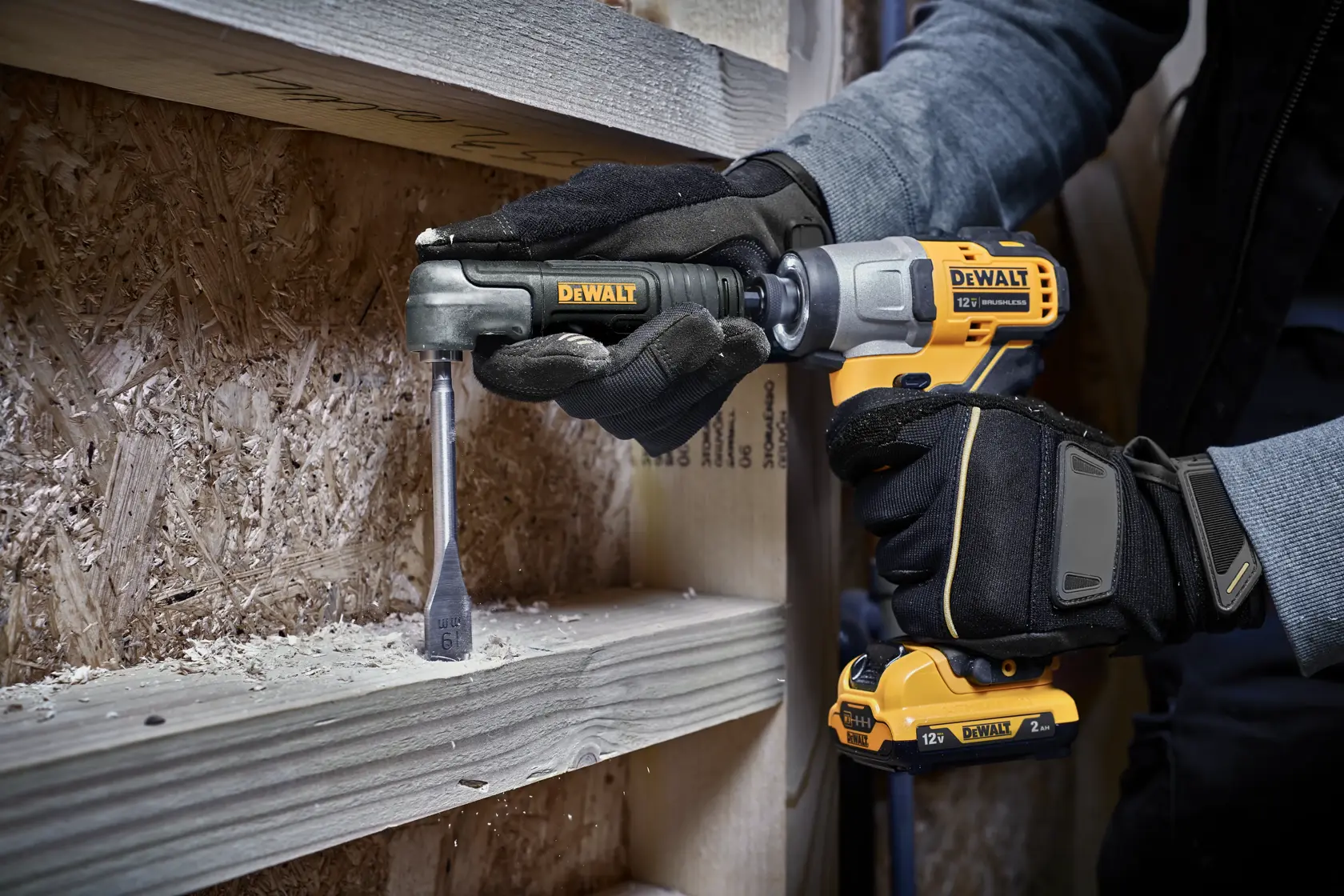 A person wearing black gloves uses a yellow DEWALT cordless drill with a right angle attachment to drill into a wooden beam.