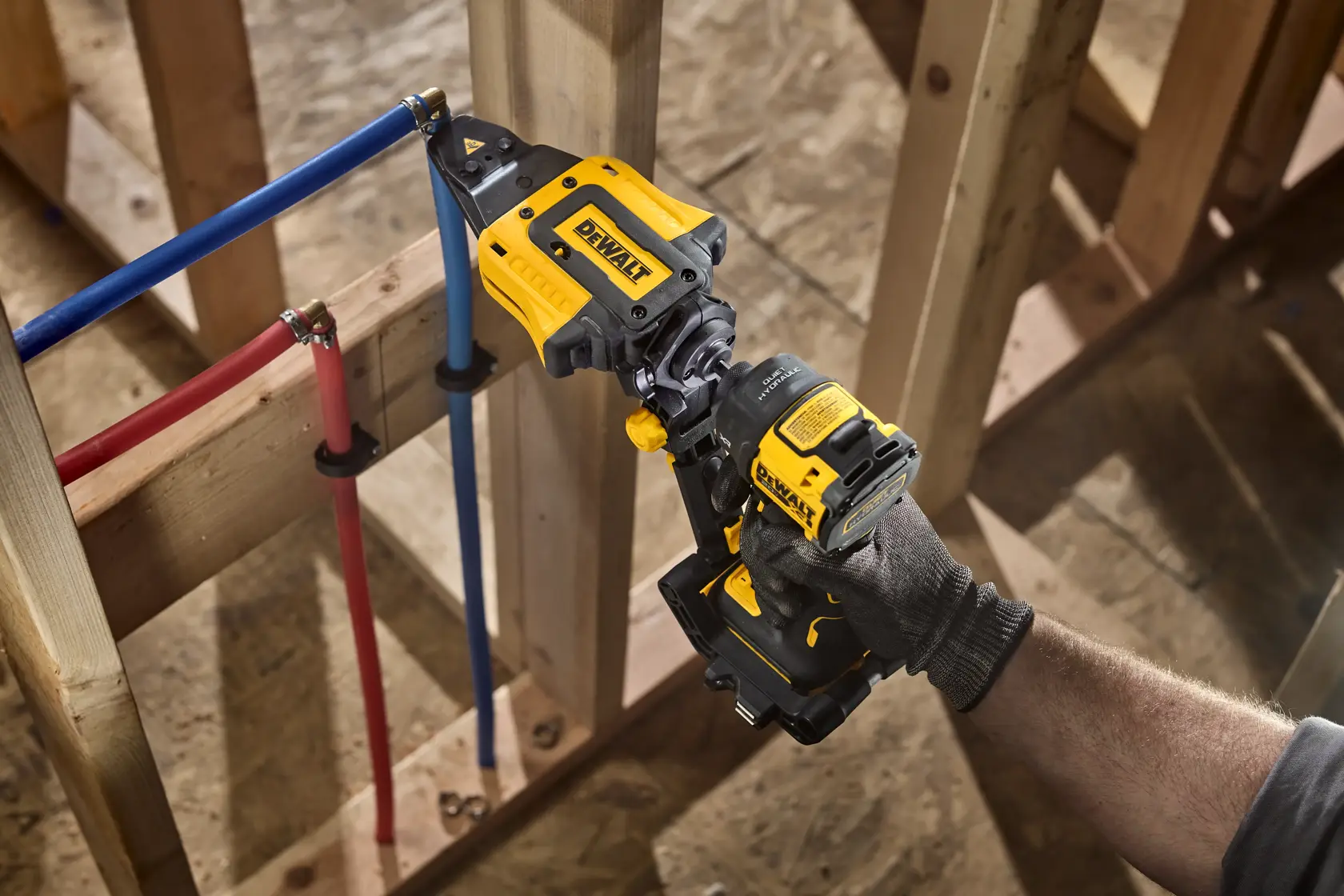 A person using a yellow and black DEWALT power tool to cut through a blue pipe attached to a wooden frame during construction.