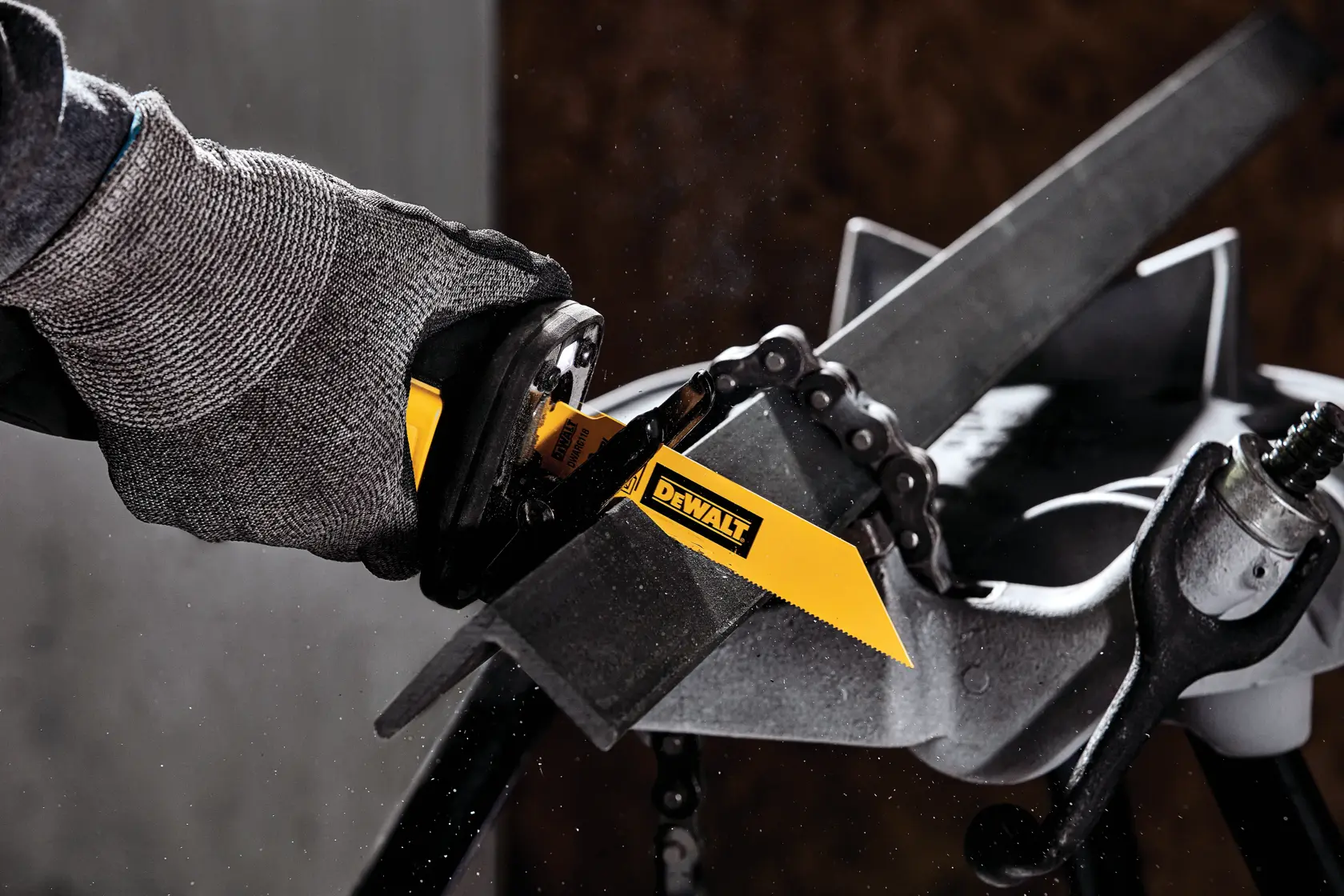 A close-up of a gloved hand using a DEWALT reciprocating saw blade to cut through a metal bar mounted in a vise.